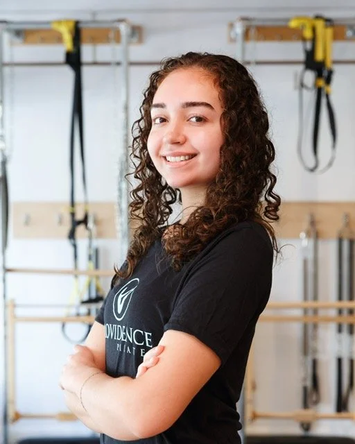 smiling woman standing in Providence Pilates studio posing for a headshot with arms crossed