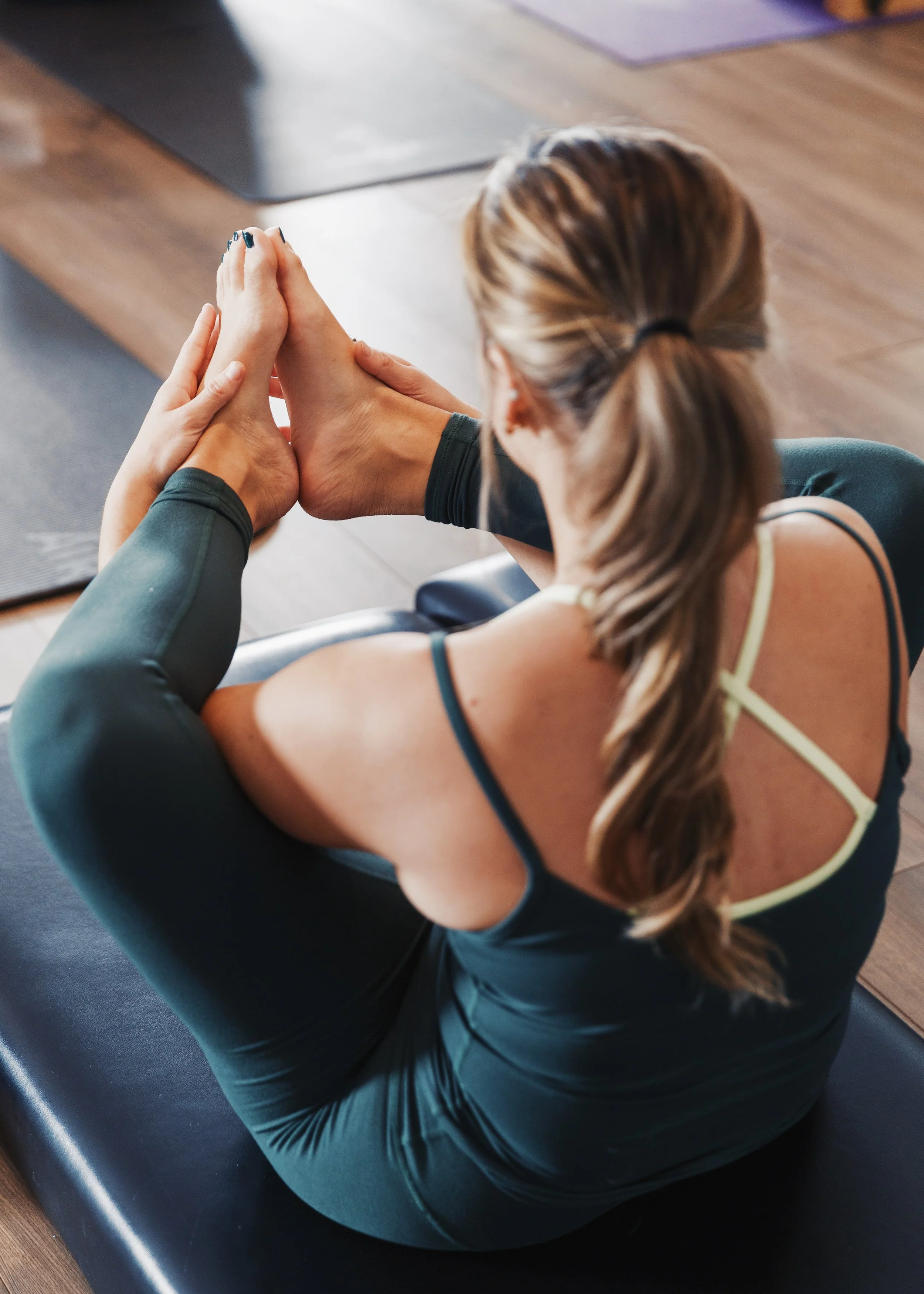 Woman in activewear on a yoga mat, holding her feet and stretching in a seated pose doing power pilates  in Providence, Rhode Island.