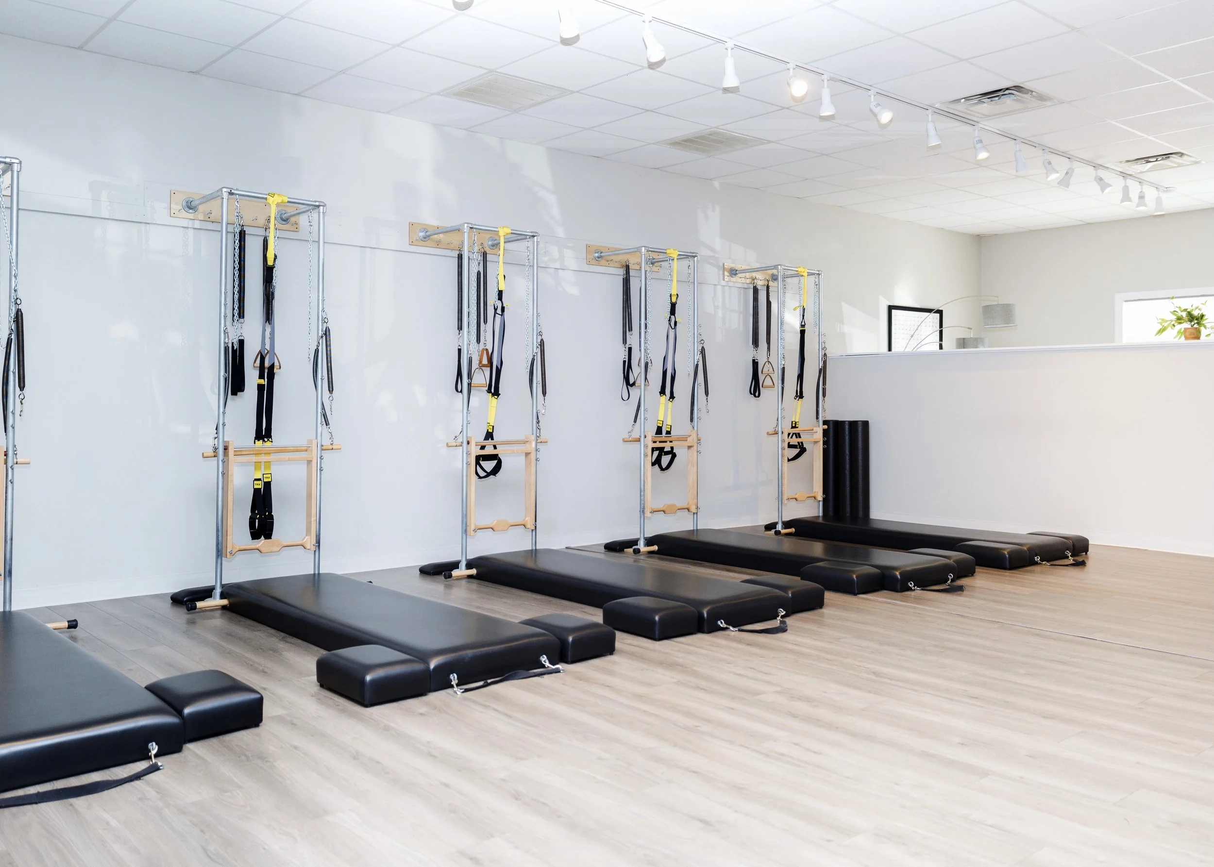 A bright Power Pilates Providence studio with six reformer mats and wall-mounted resistance bands on a light wooden floor.