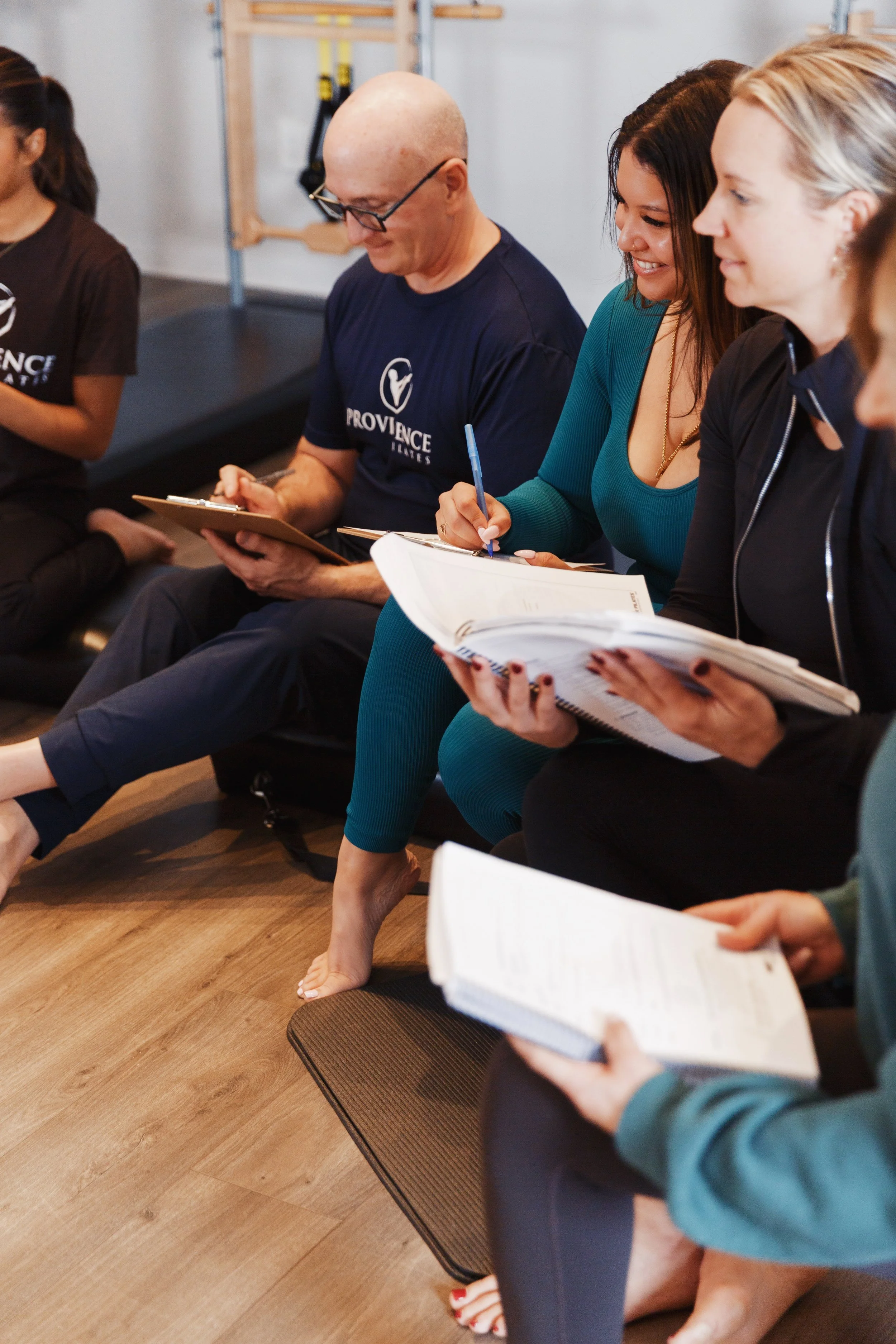 pilates instructors sitting in a studio with notebooks during a training session
