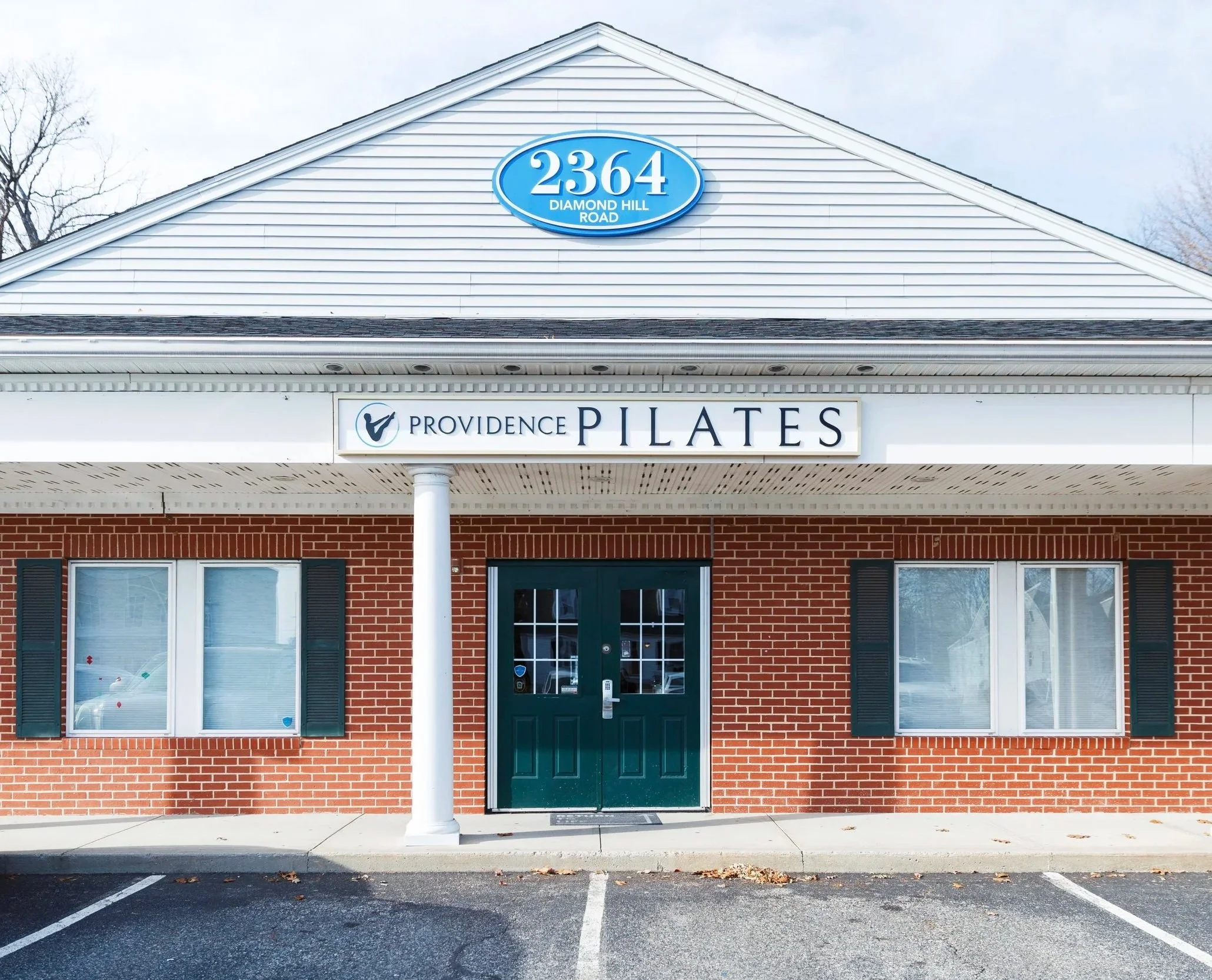 Red brick building with white columns and white roof, housing the Providence Pilates Center studio in Cumberland Rhode Island. Address sign reads 2364 Diamond Hill Road in light blue and white.