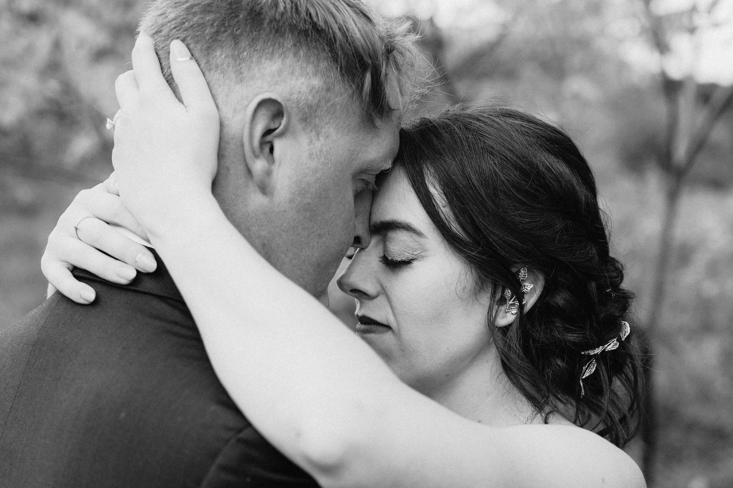 A black and white photo of a couple embracing with their foreheads touching, eyes closed, and faces close together.