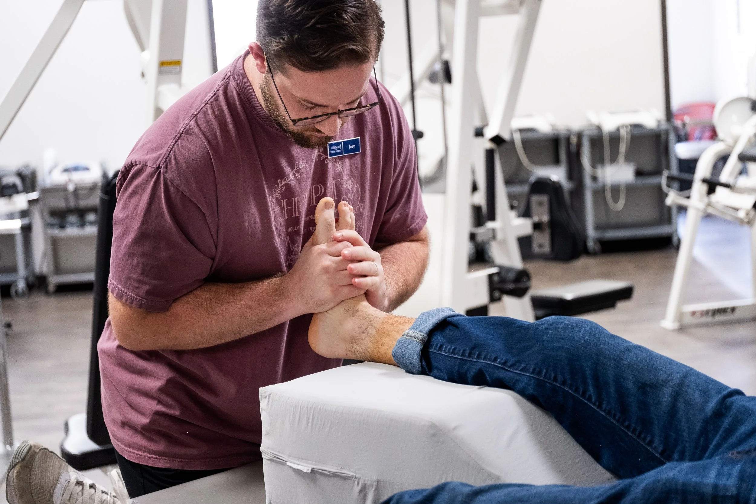 Physical therapist performing ankle therapy on a patient lying on a treatment table in a rehabilitation clinic.