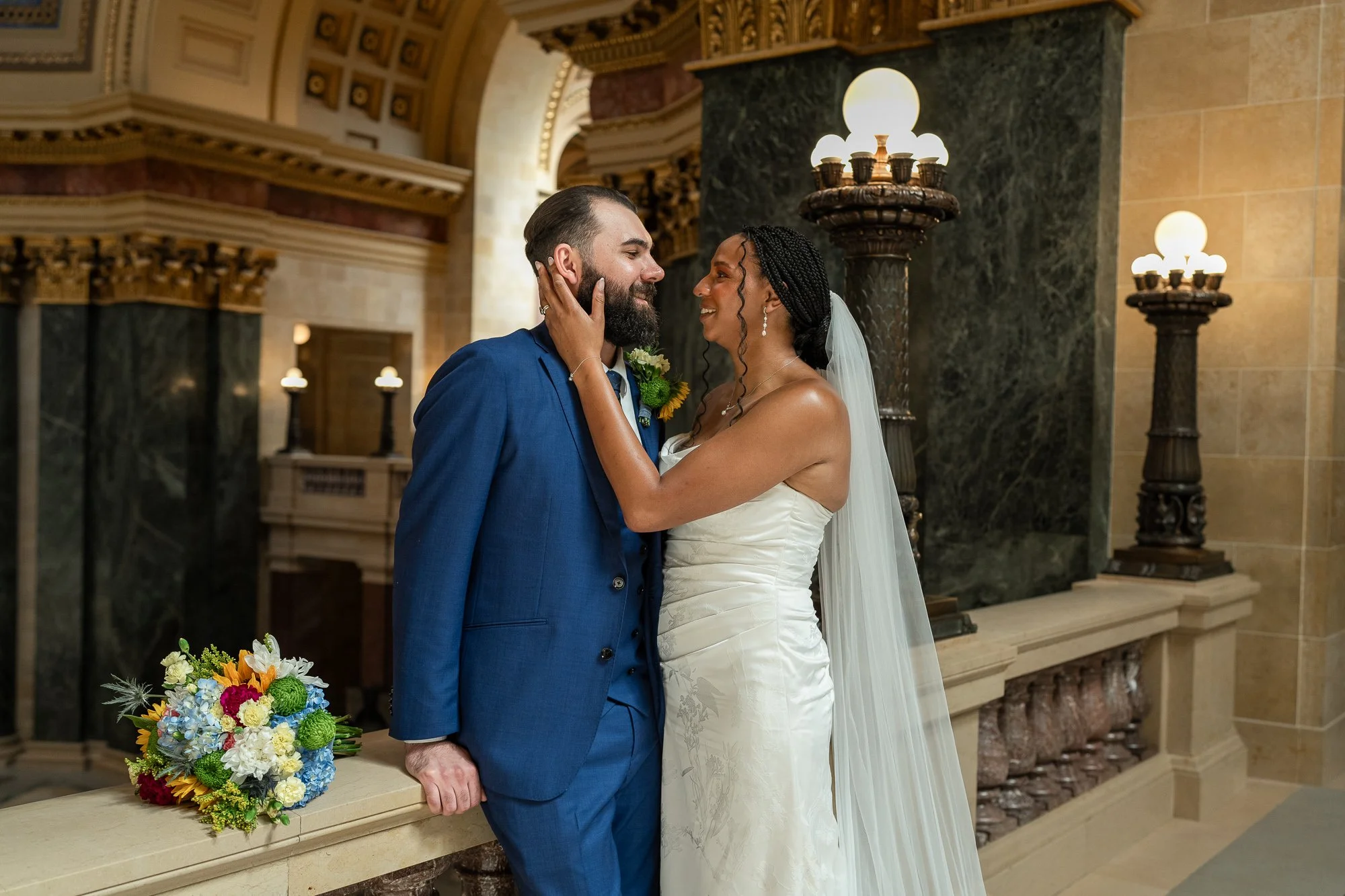 Wedding bouquet on ledge of state capital as wedding couple embraces.