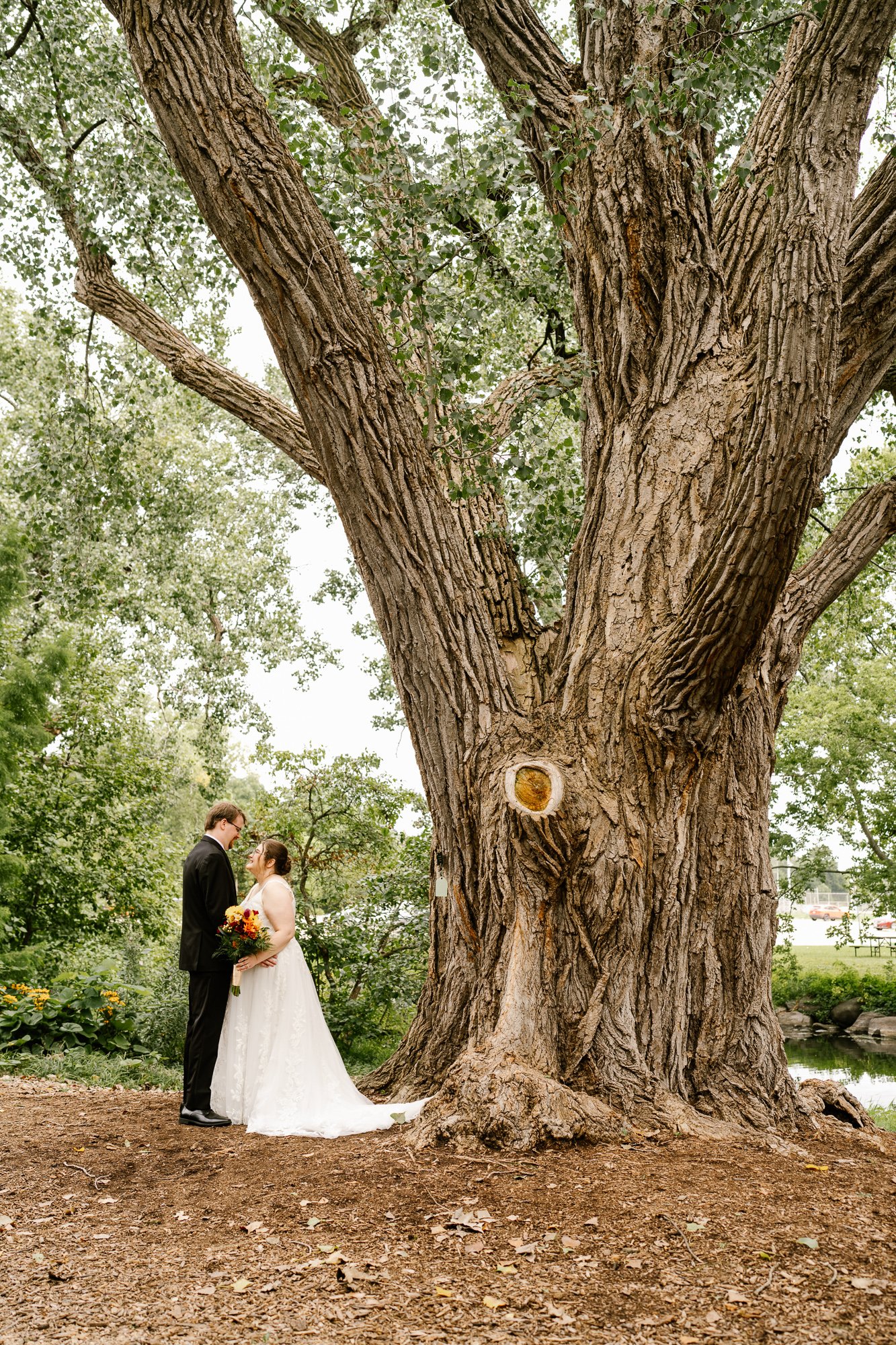 Bride and groom standing beneath a large tree at Olbrich Botanical Gardens in Madison, Wisconsin