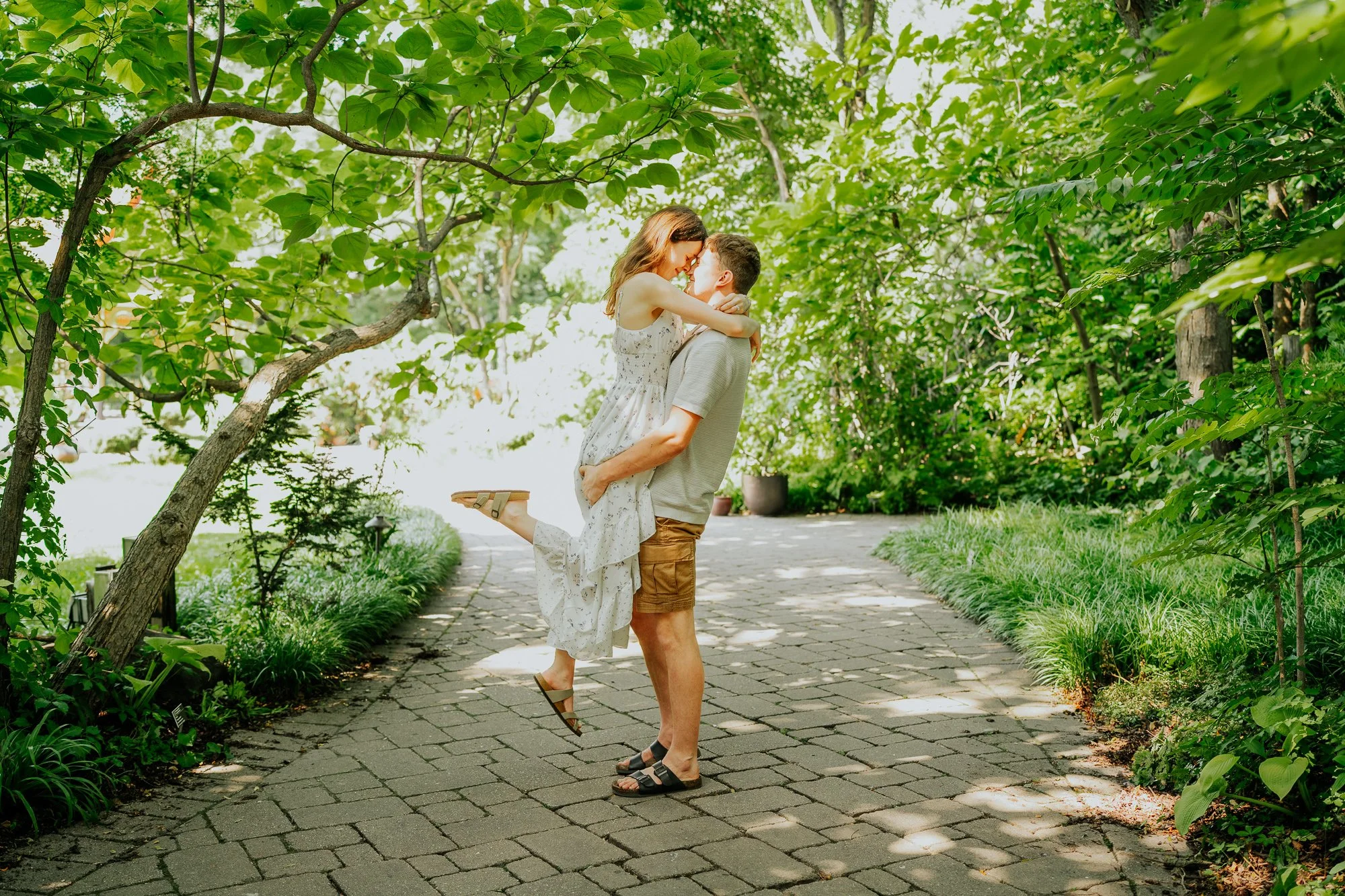 Man lifting his fiancée beneath the trees at Olbrich Botanical Gardens