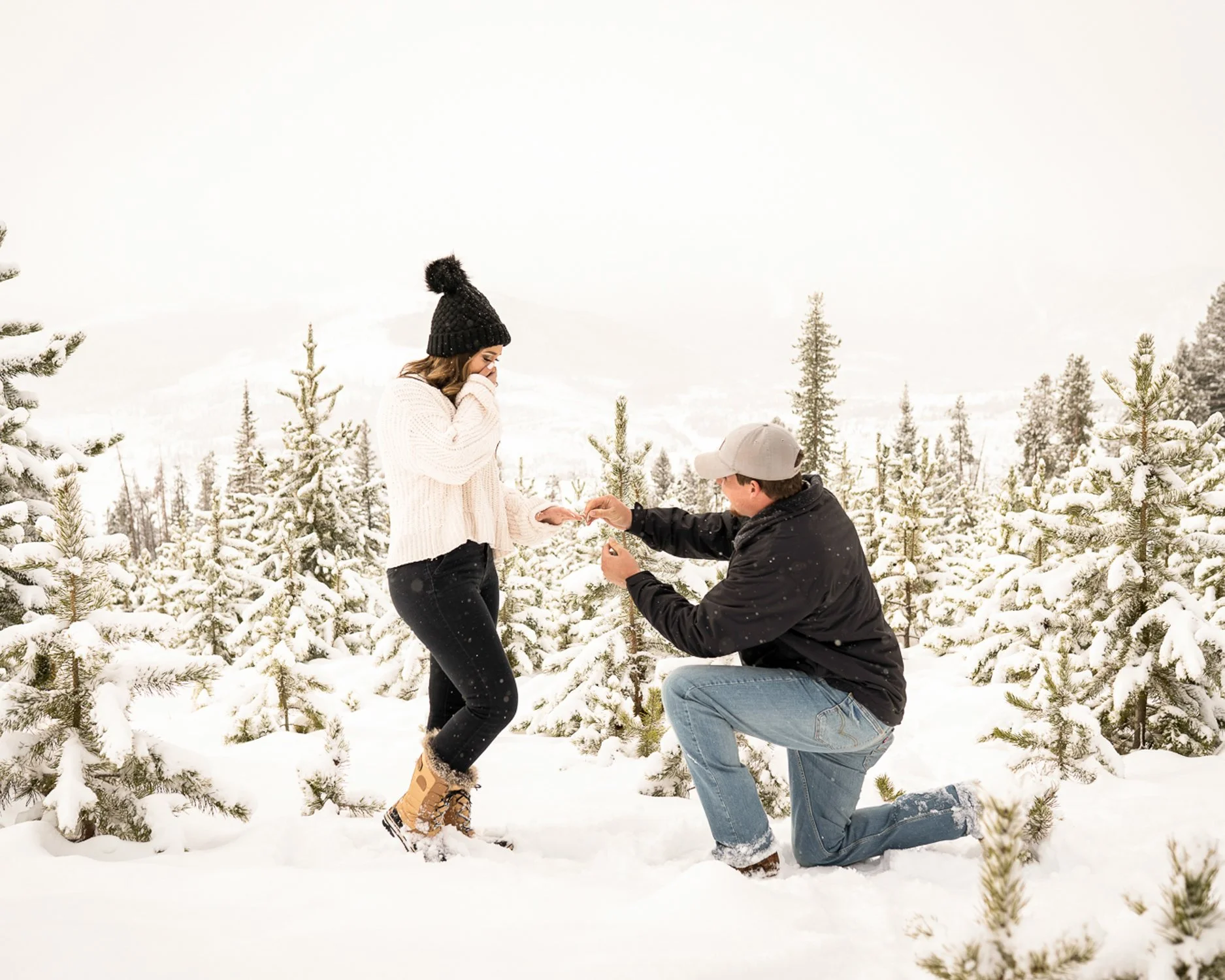A man proposes marriage to a woman in a snowy forest, holding her hand.