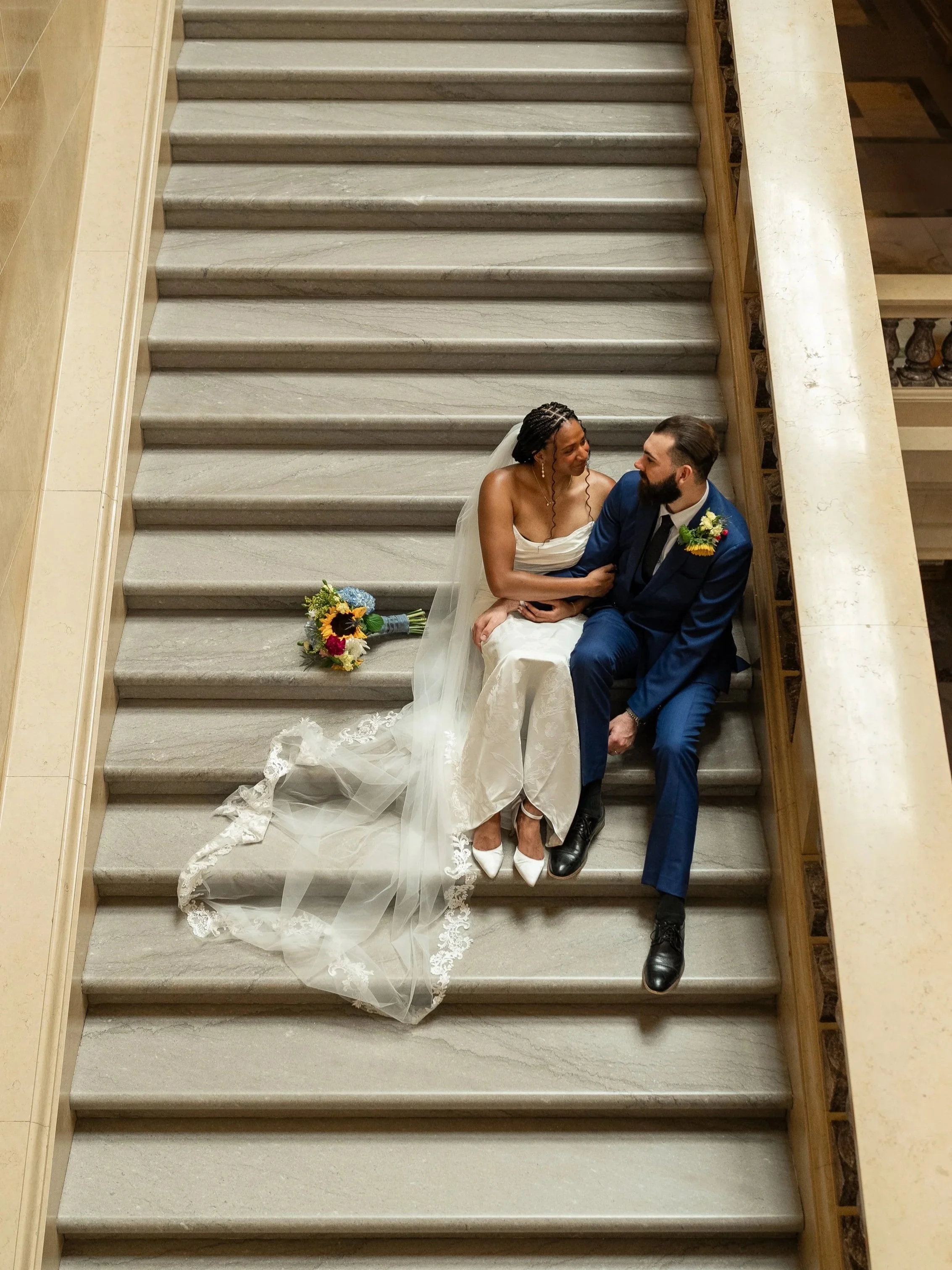 Bride and groom sitting together on a marble staircase inside the Wisconsin State Capitol in Madison.