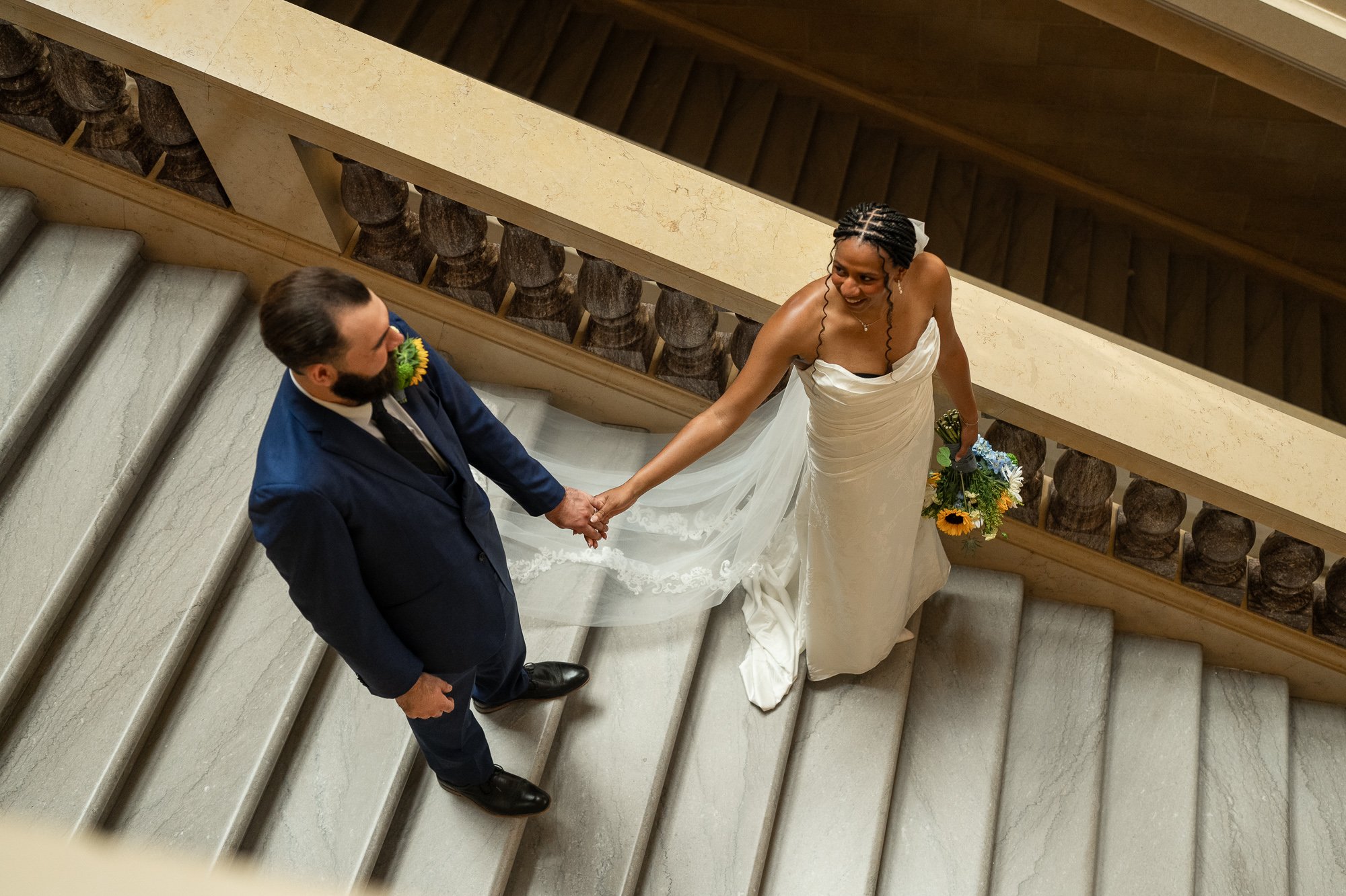 Women in wedding dress reaches for her grooms hand on stairway in state capital.