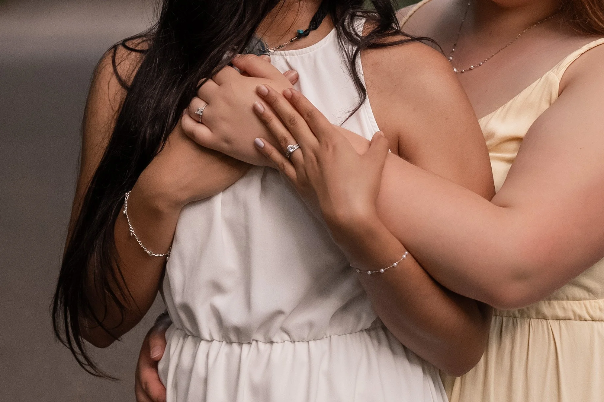 Two women dressed in cream-colored and white dresses embrace at an event.