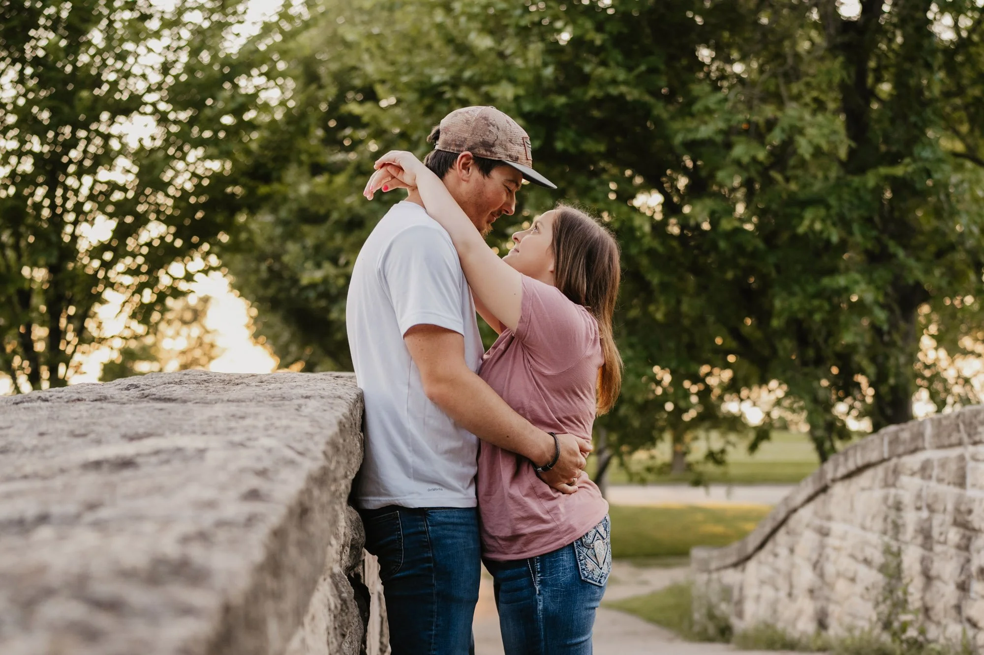 A couple embracing on a stone bridge outdoors at sunset, looking into each other's eyes.