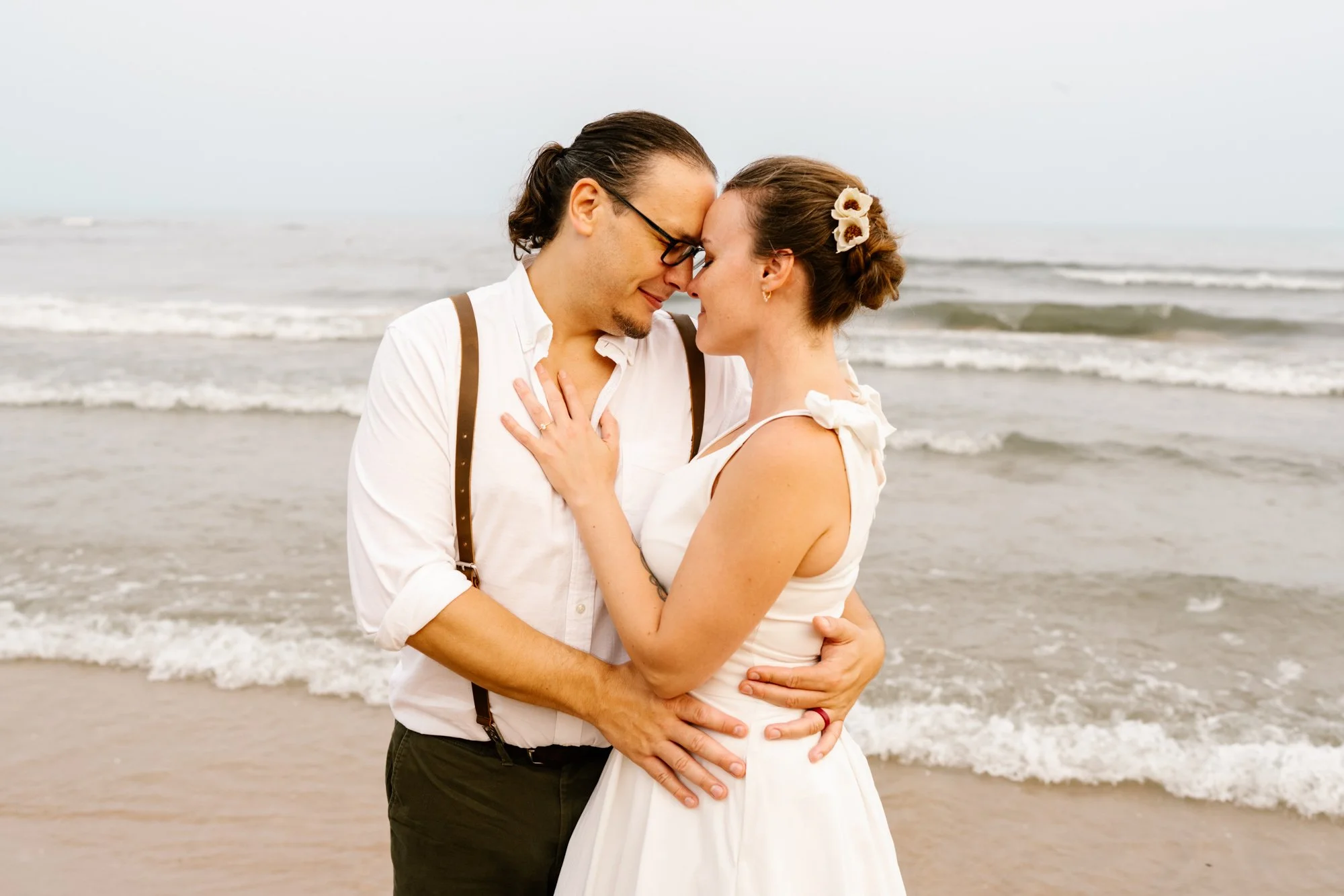 A couple in wedding attire sharing a kiss on the beach, with the ocean waves in the background.