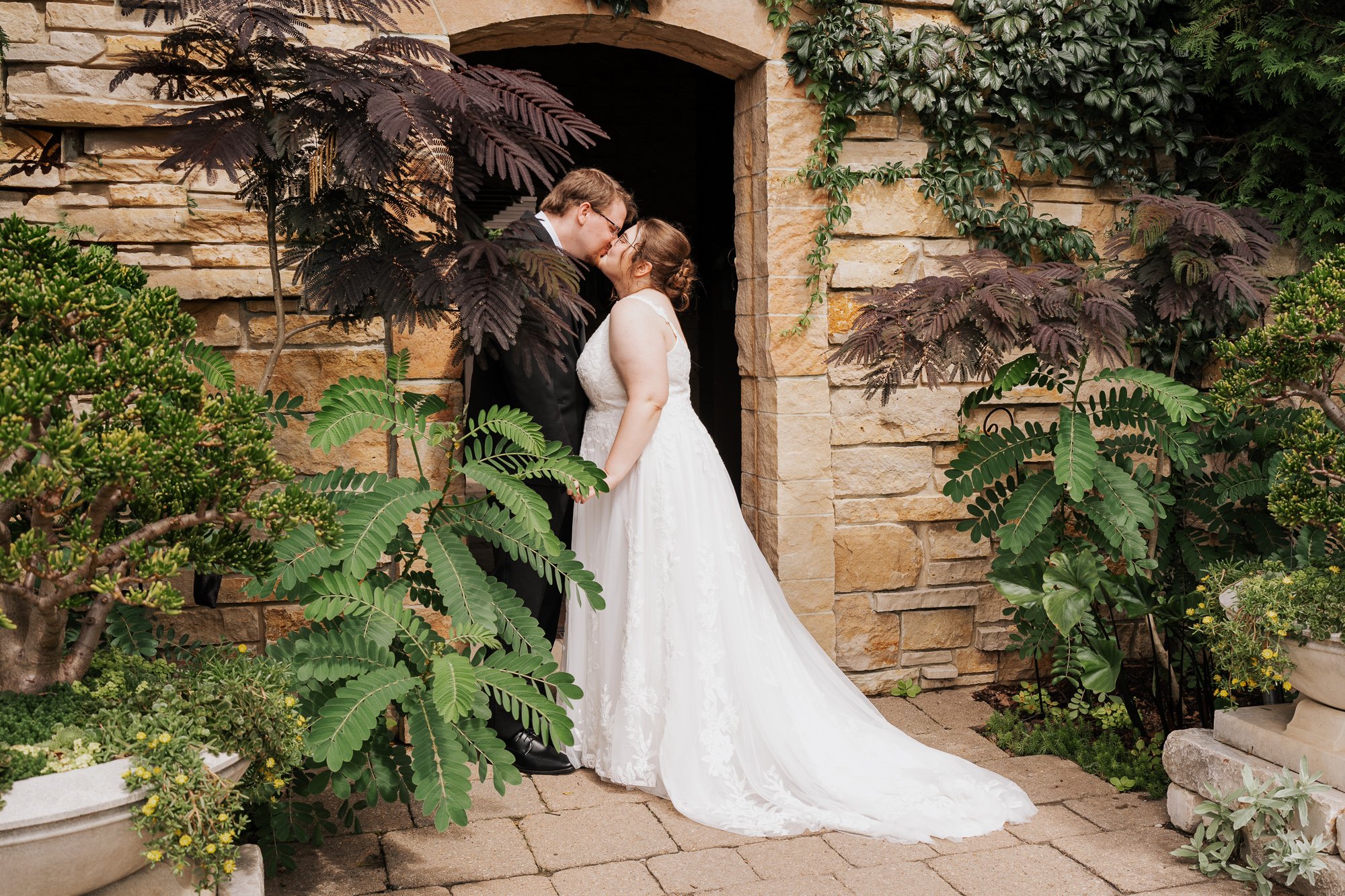 Bride and groom kissing beneath a stone archway at Olbrich Botanical Gardens