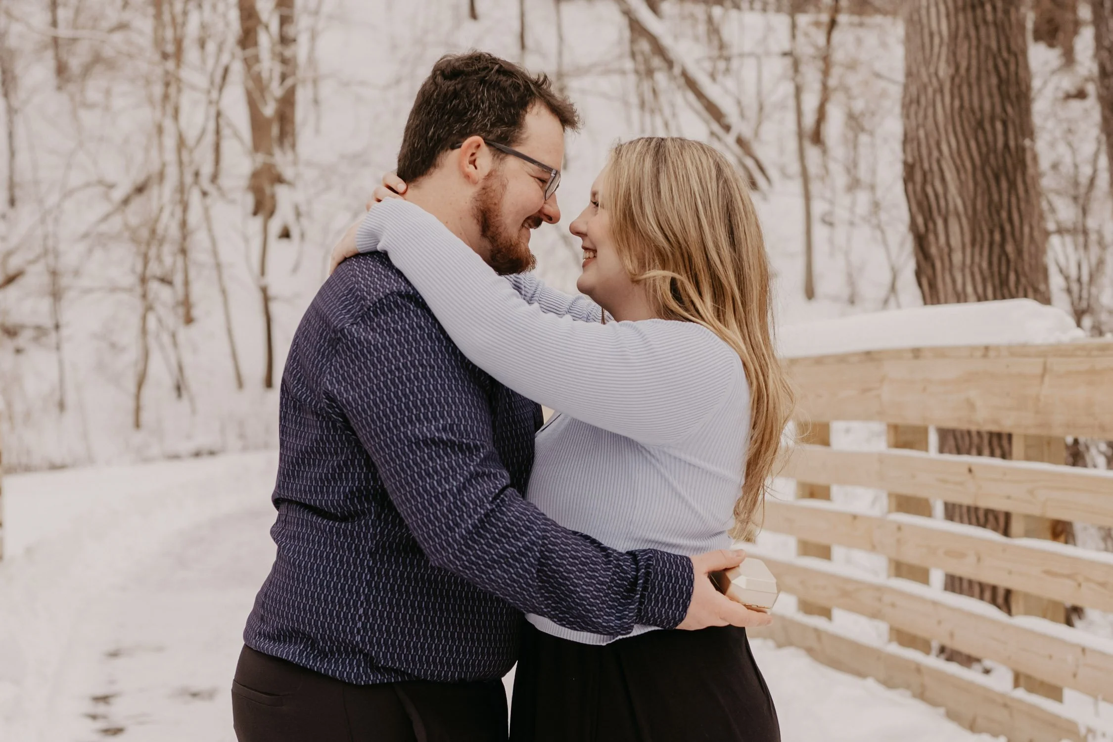 A couple matching smiles as they embrace each other in a snowy outdoor setting during winter.