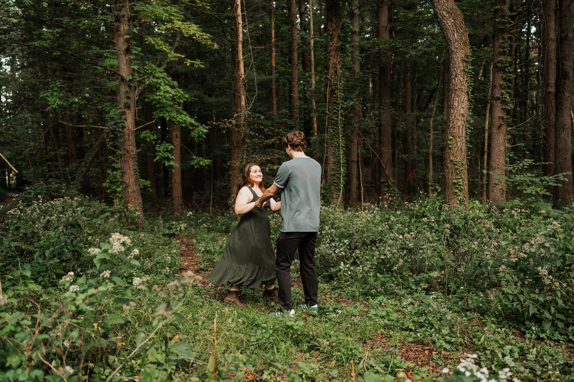 Couple dancing together through a wooded trail at the UW–Madison Arboretum during their engagement session.