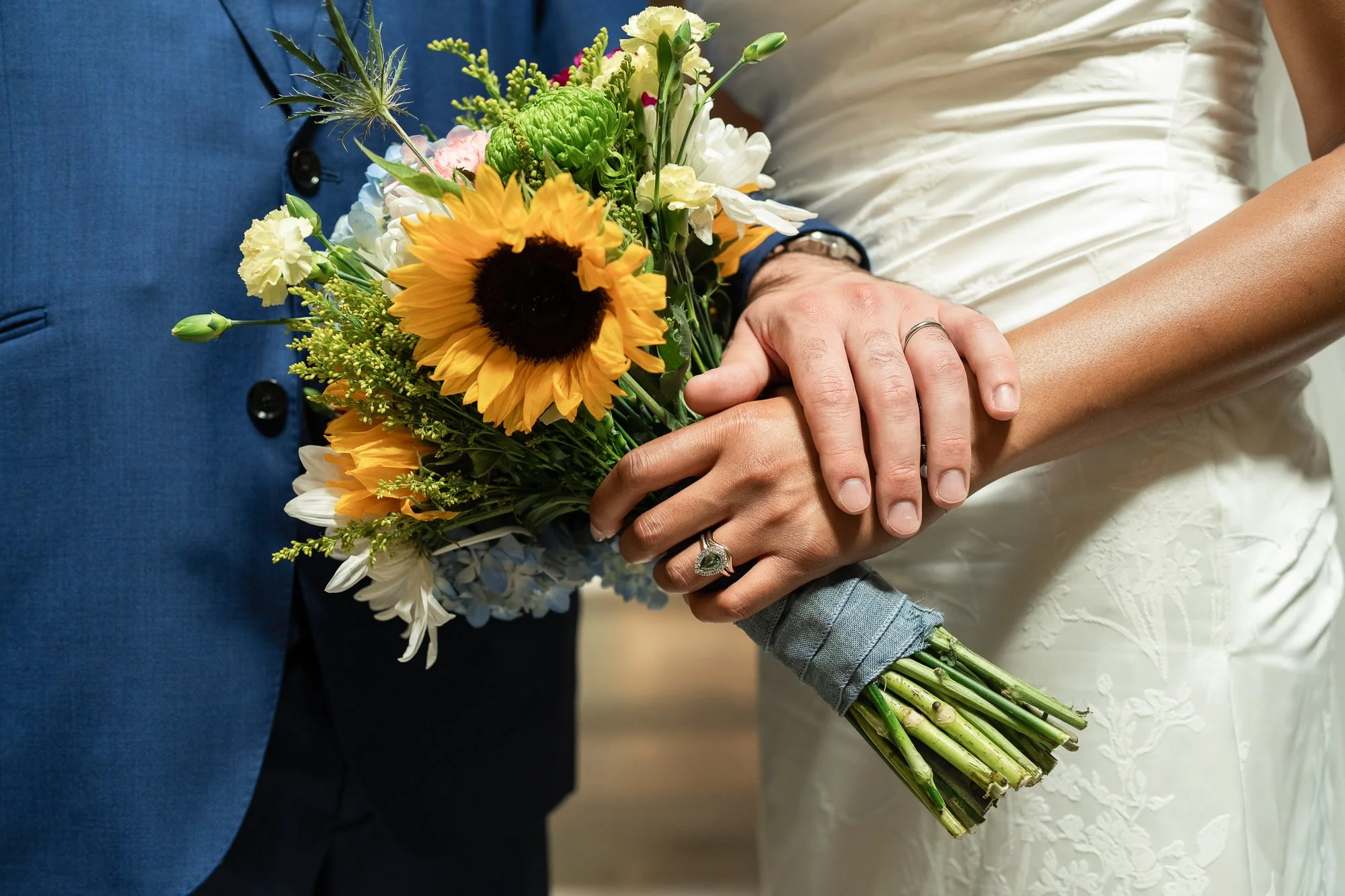 Close up of wedding rings while holding flow bouquet featuring a sunflower.