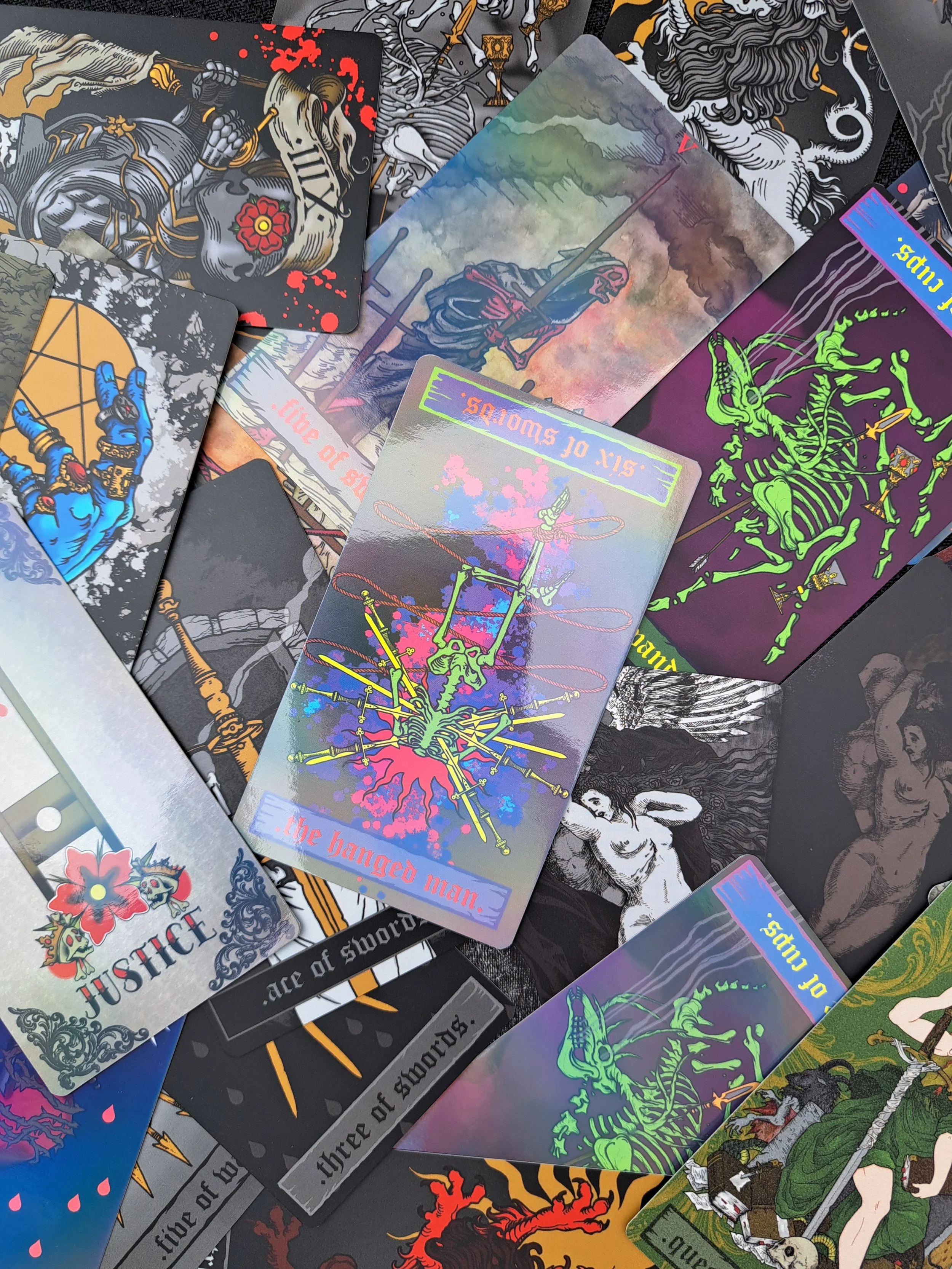 A collection of tarot cards with various bright illustrations, a knight, a skeleton, a guillotine, a deer and a blue hand holding a pentagram.