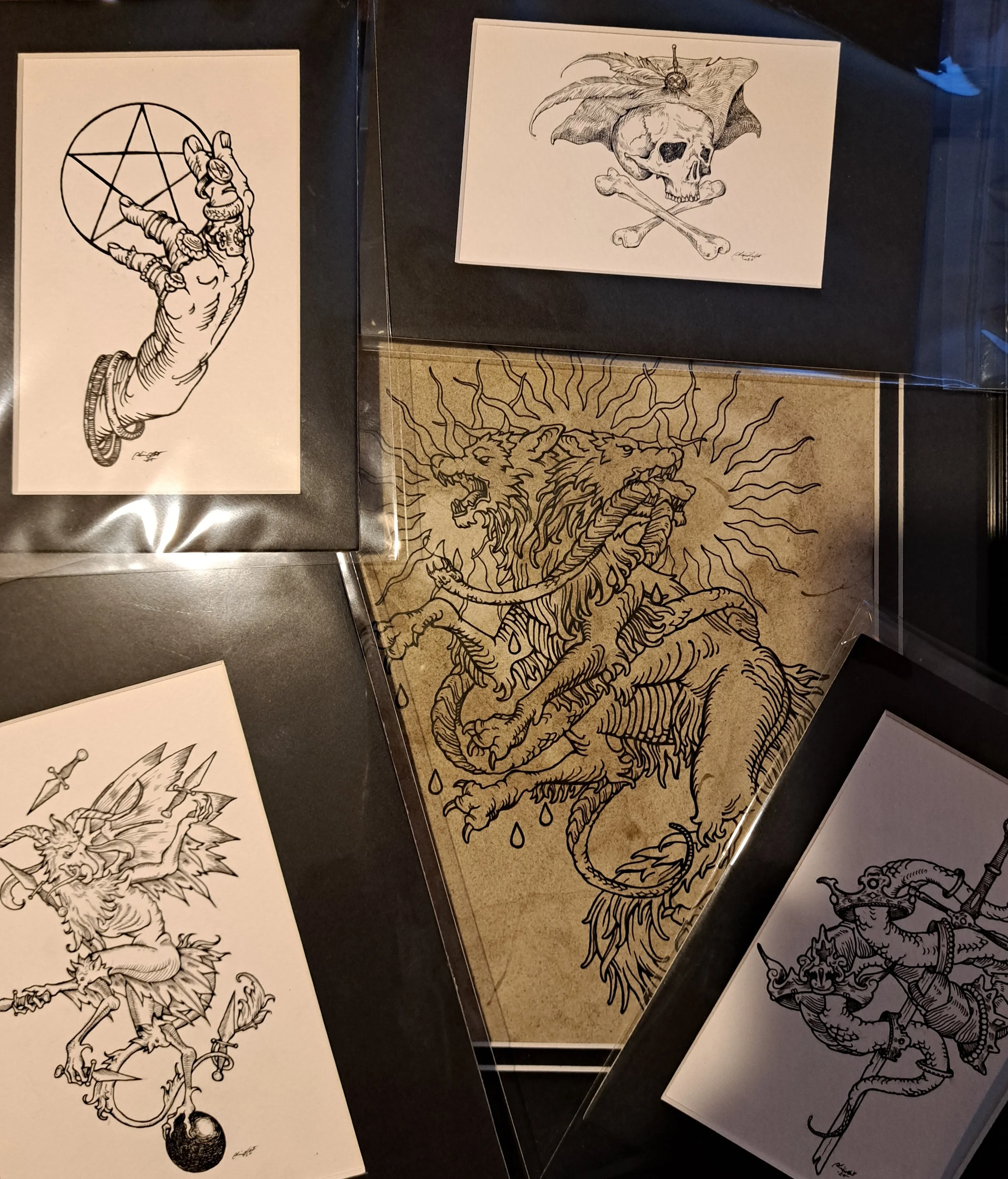 Collection of five black-and-white fantasy and mystical-themed drawings including a hand with a pentagram, a skull with crossbones and a leaf, a two-headed lion with radiating lines, a crowned monkey with a staff, and a creature with equine and reptilian features.
