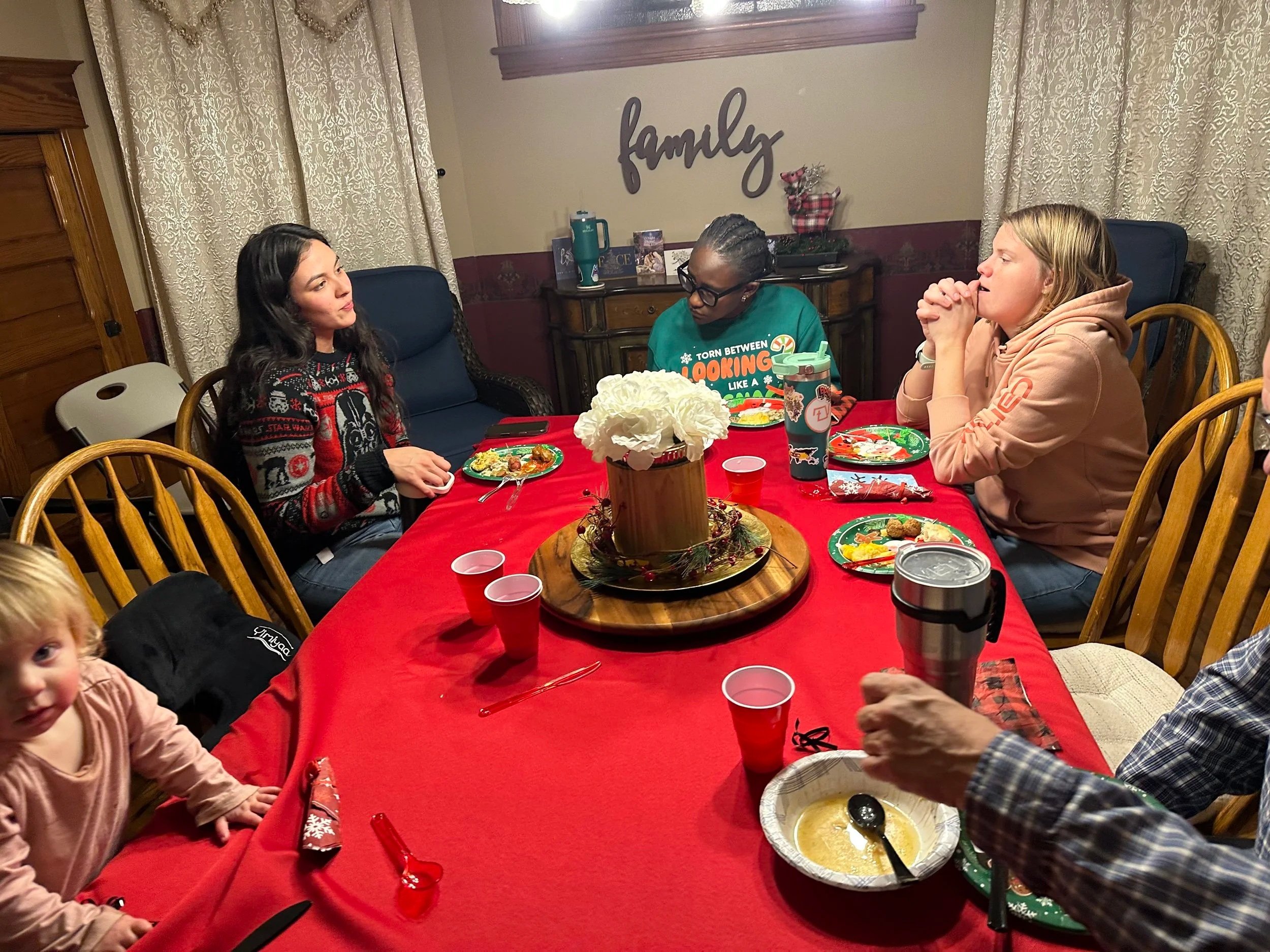 Family gathered around a table for a meal, with some plates of food, cups, and decorations, in a cozy dining room.