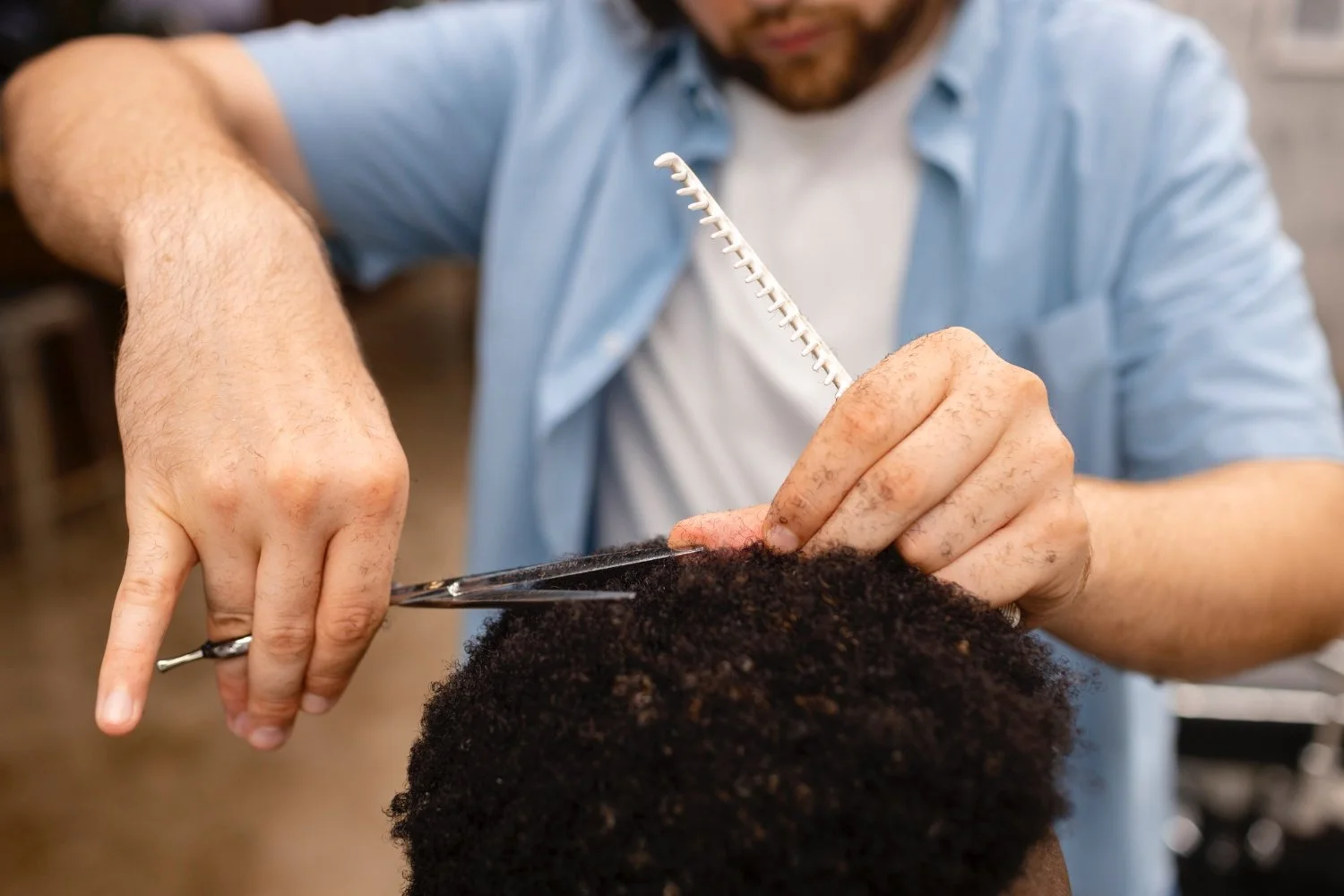 Un homme coupe les cheveux d'une personne à l'aide de ciseaux. La personne dont il coupe les cheveux a des cheveux afro noirs.