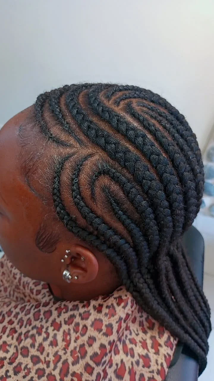 Coiffure avec des tresses en lignes courbes géométriques sur la tête d'une personne, coiffée de cheveux noirs.