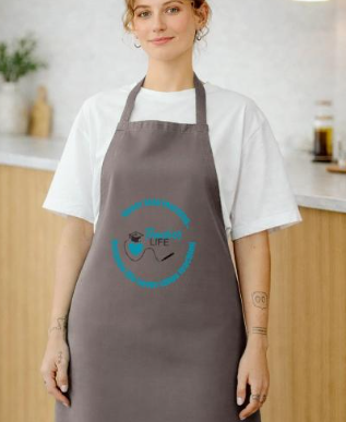 A young woman wearing a white t-shirt and gray apron in a kitchen setting.