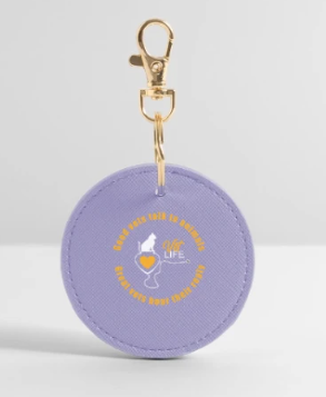 Purple circular keychain with yellow text and a white heart design, attached to a gold clip.