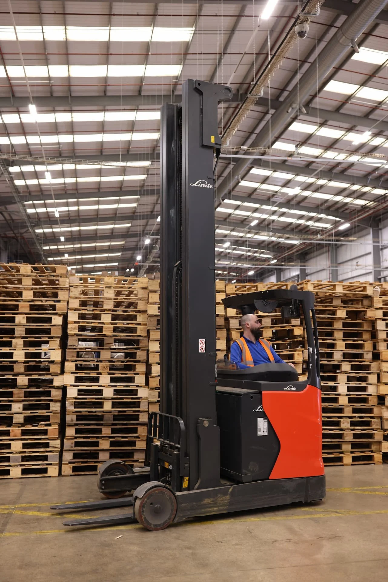A man operating a forklift in a warehouse with wood pallets stacked in the background.