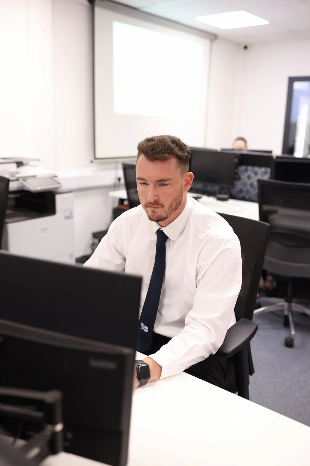 Man in white shirt and navy tie working at his computer in an office.