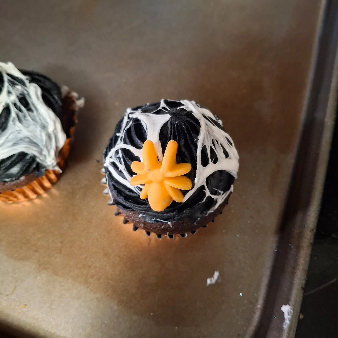 Halloween cupcake decorated with black and white icing and an orange candy in the shape of a spider or star on top.