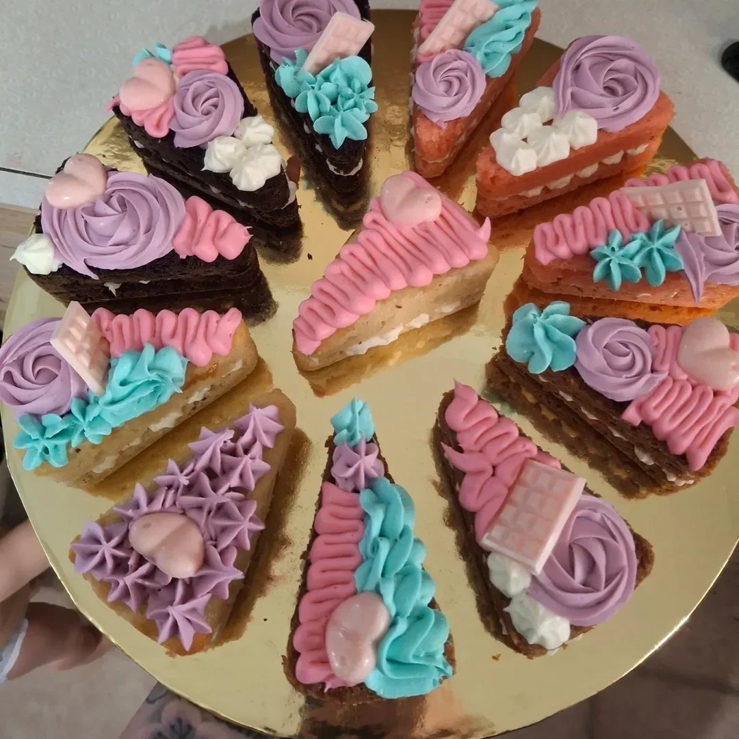 Assorted slices of decorated cakes with pink, purple, blue, and white frosting on a gold tray.