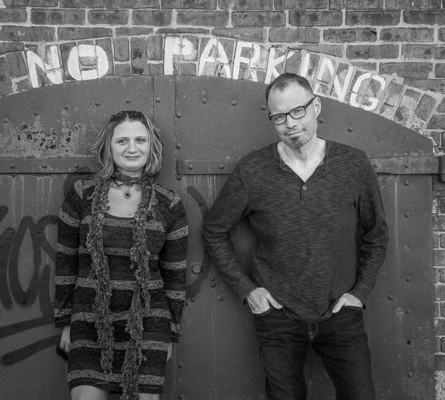 A woman and a man standing in front of a brick wall with a metal gate that has a 