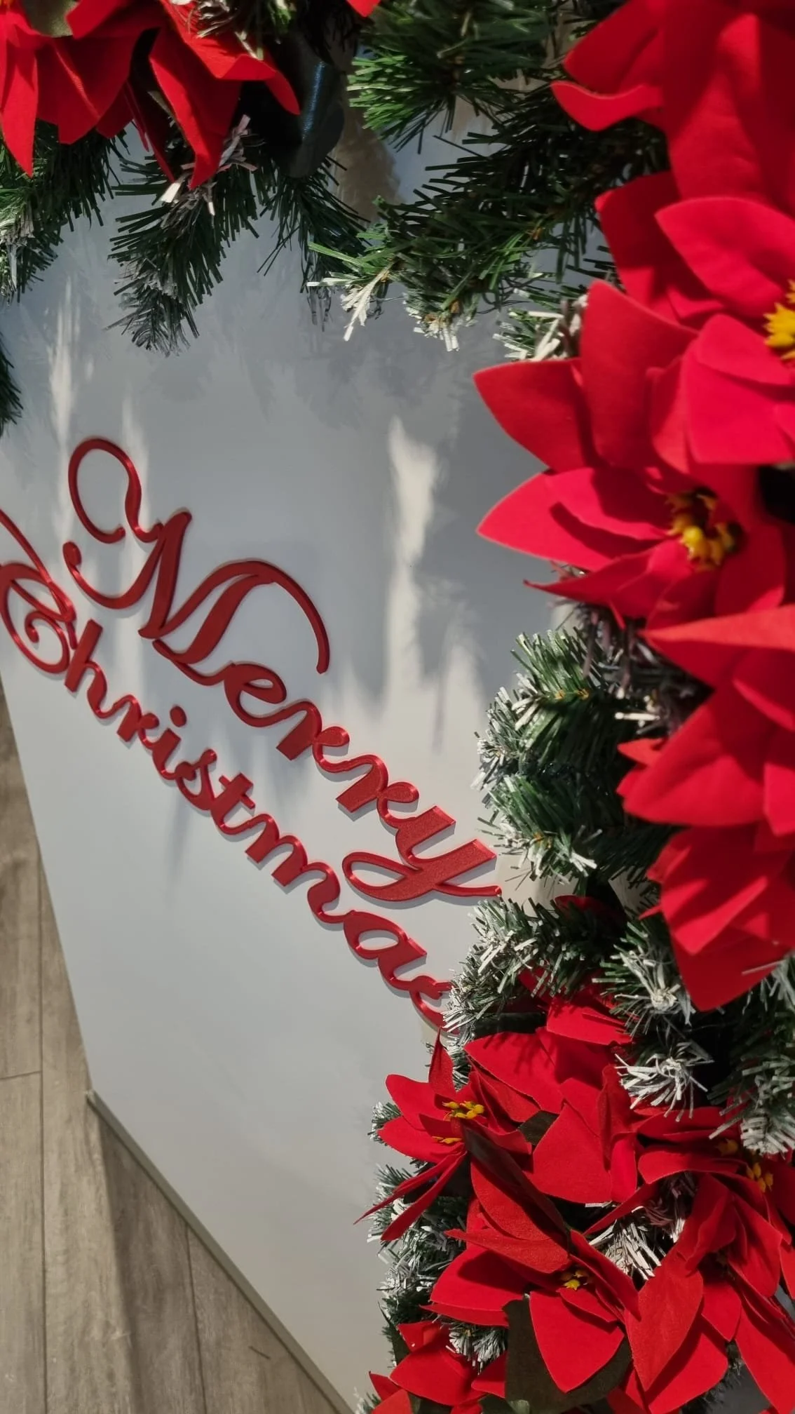 Christmas decoration with red poinsettias, green pine branches, and a red 'Merry Christmas' sign.