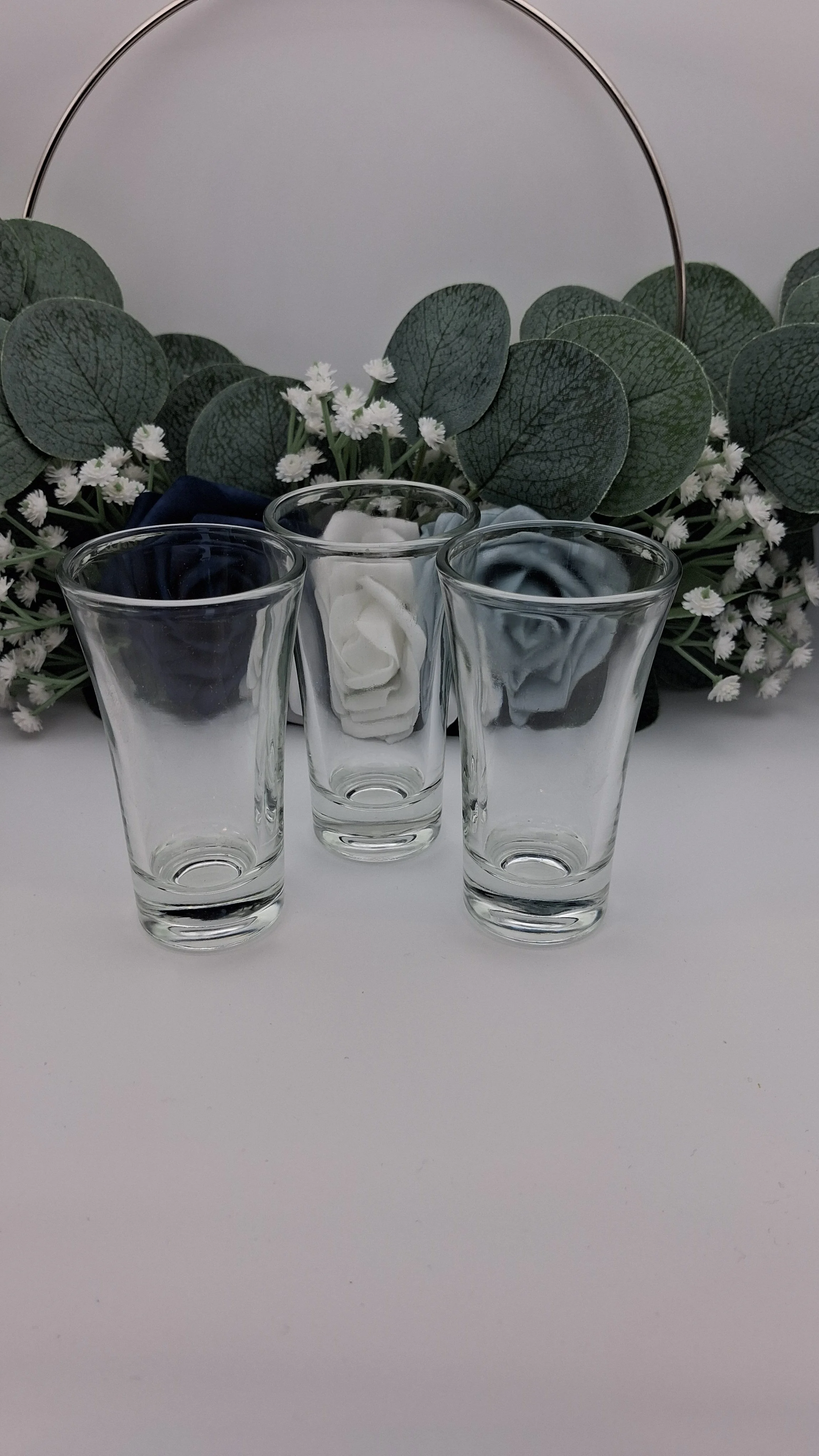3 50ml shot glasses arranged in front of blue flowers