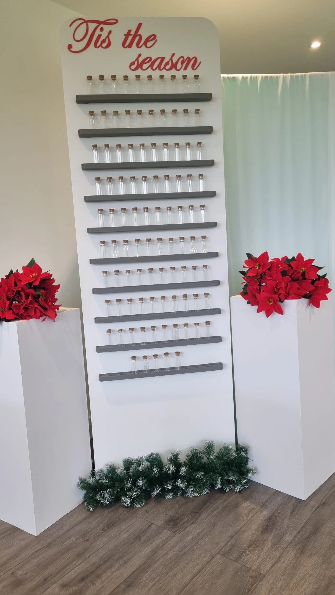 Display sign with empty glass bottles on shelves, decorated for the holiday season with Christmas poinsettias and greenery.