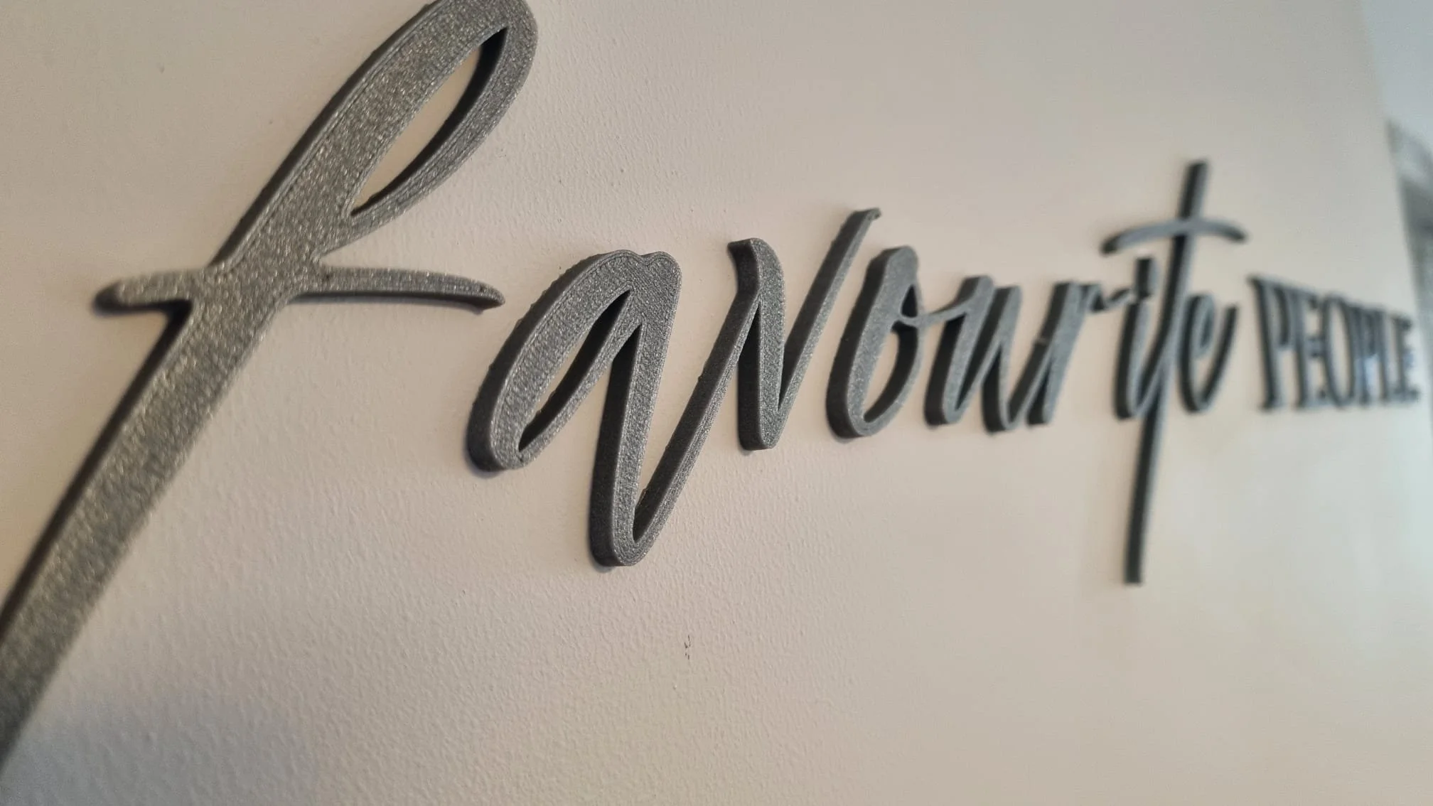 Close-up of metallic 3D text on a wall that says "If Now You Feel" with a beige wall background.