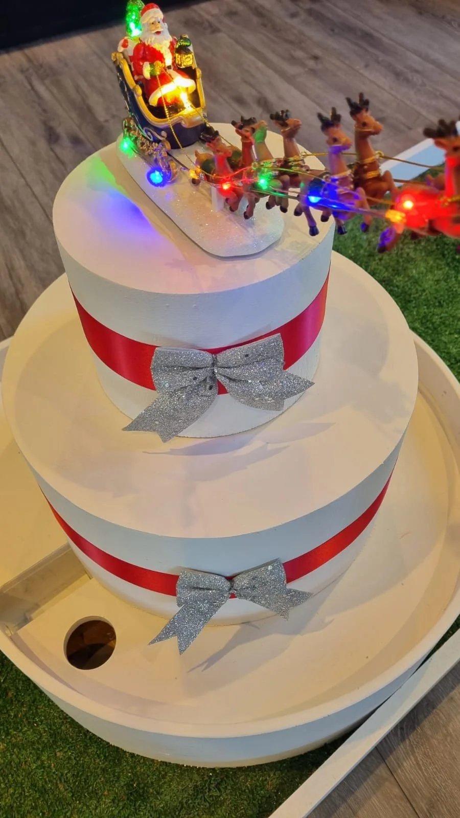 Christmas cake with Santa in a sleigh and reindeer, decorated with colorful lights and silver bows.