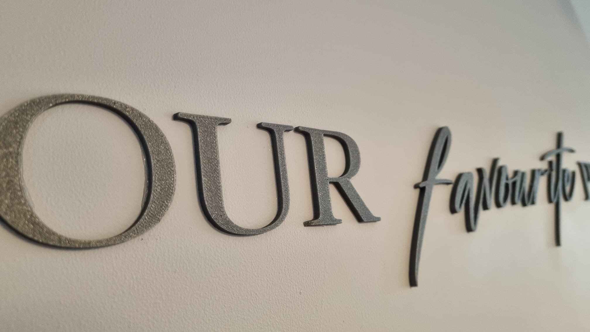 Close-up of wall decor spelling out part of the phrase 'OUR tomorrow' in metallic black and silver letters.