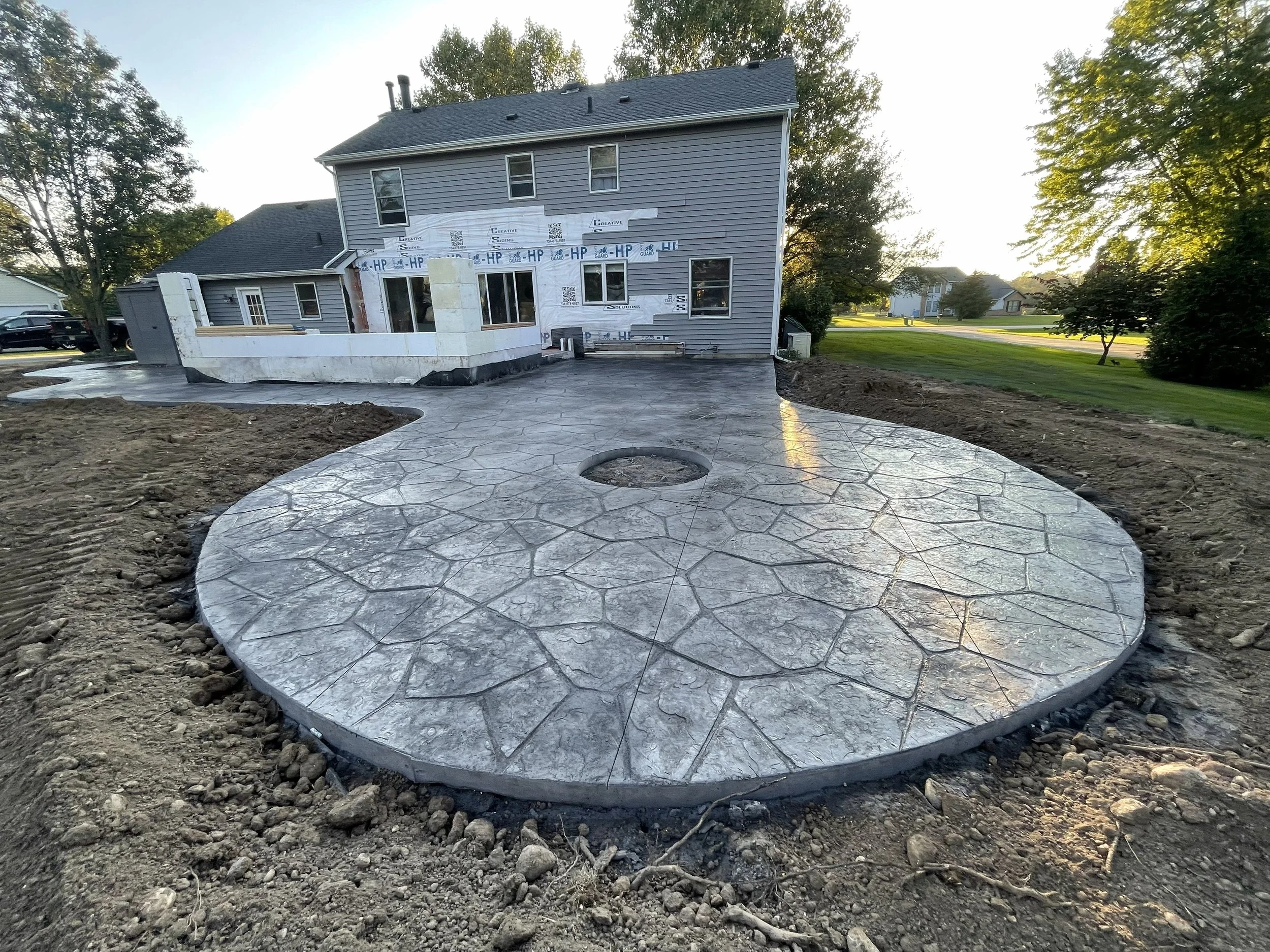 Finished concrete patio with a decorative stone pattern in the backyard of a house under construction.