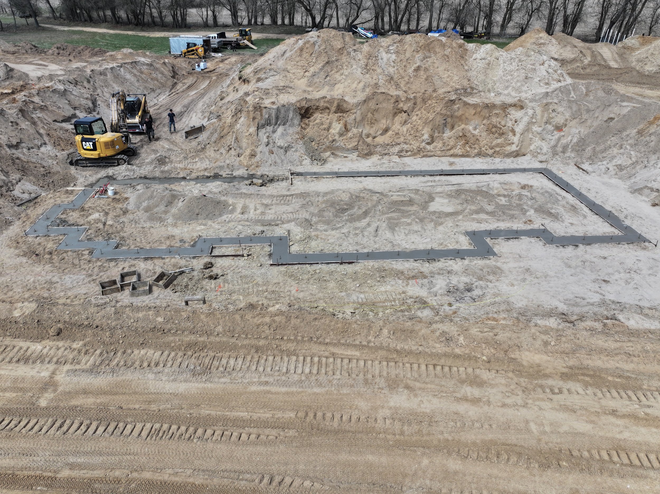 Construction site with foundations being laid, a small excavator, and construction workers.