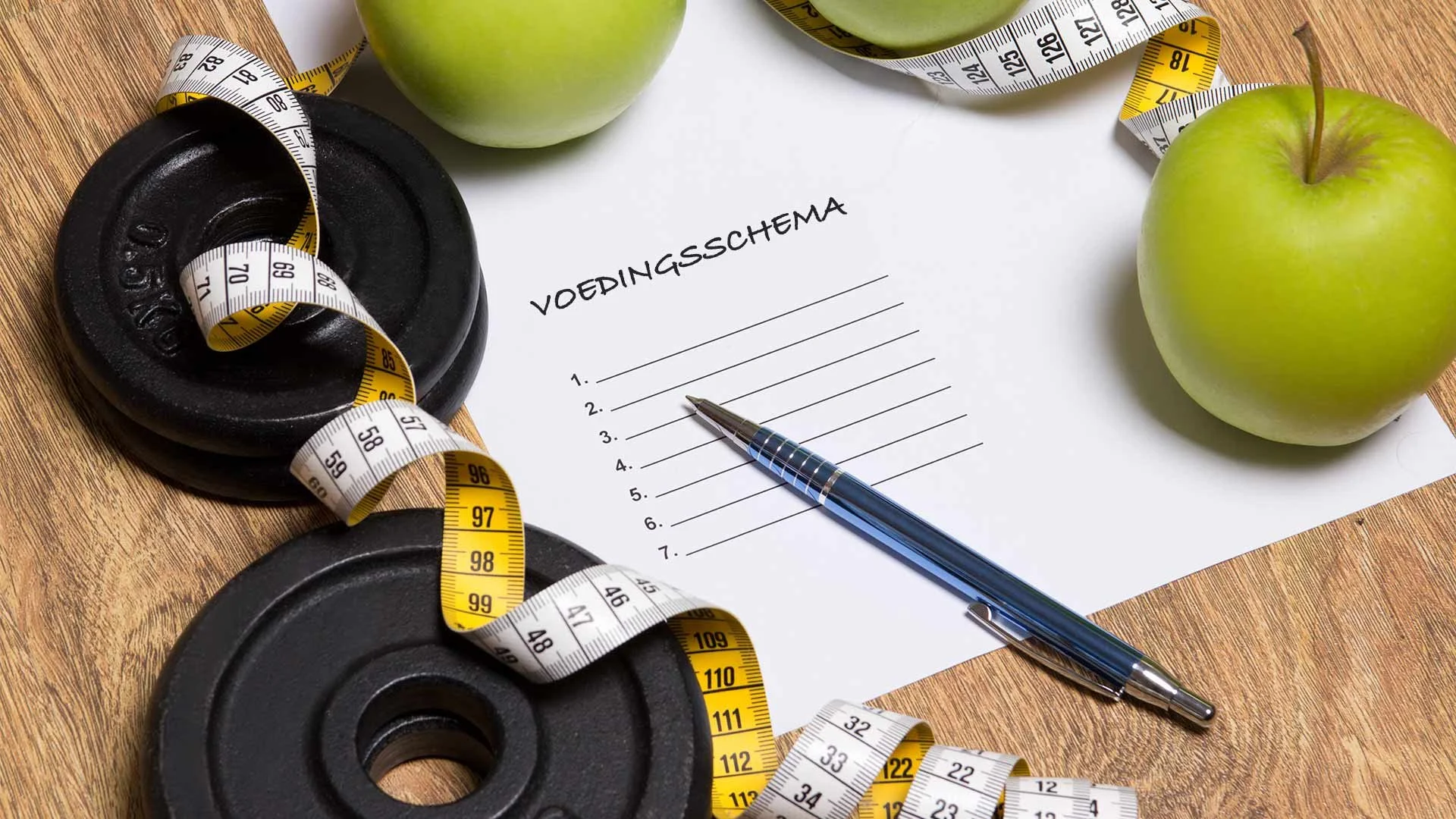 Waterschema op een wit blad met een pen, groene appels, een zwart haltergewicht en een meetlint op een houten tafel.