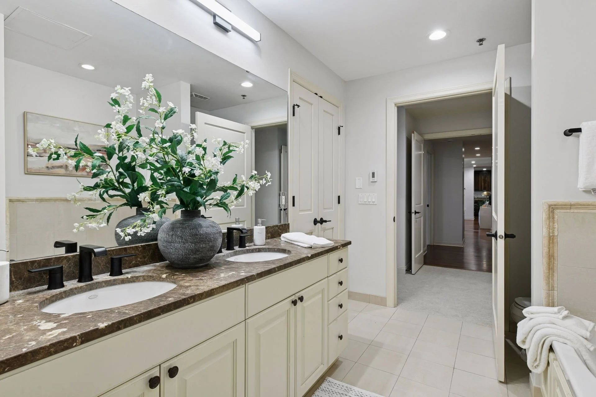A modern bathroom with a double sink vanity, marble countertop, large mirror, and black fixtures. 
