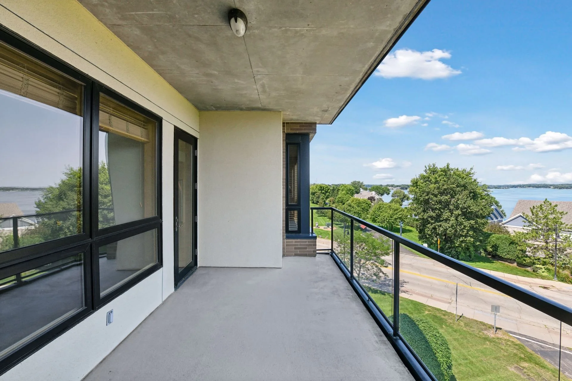 Balcony overlooking Lake Minnetonka with green trees and houses in the background, under a partly cloudy sky.