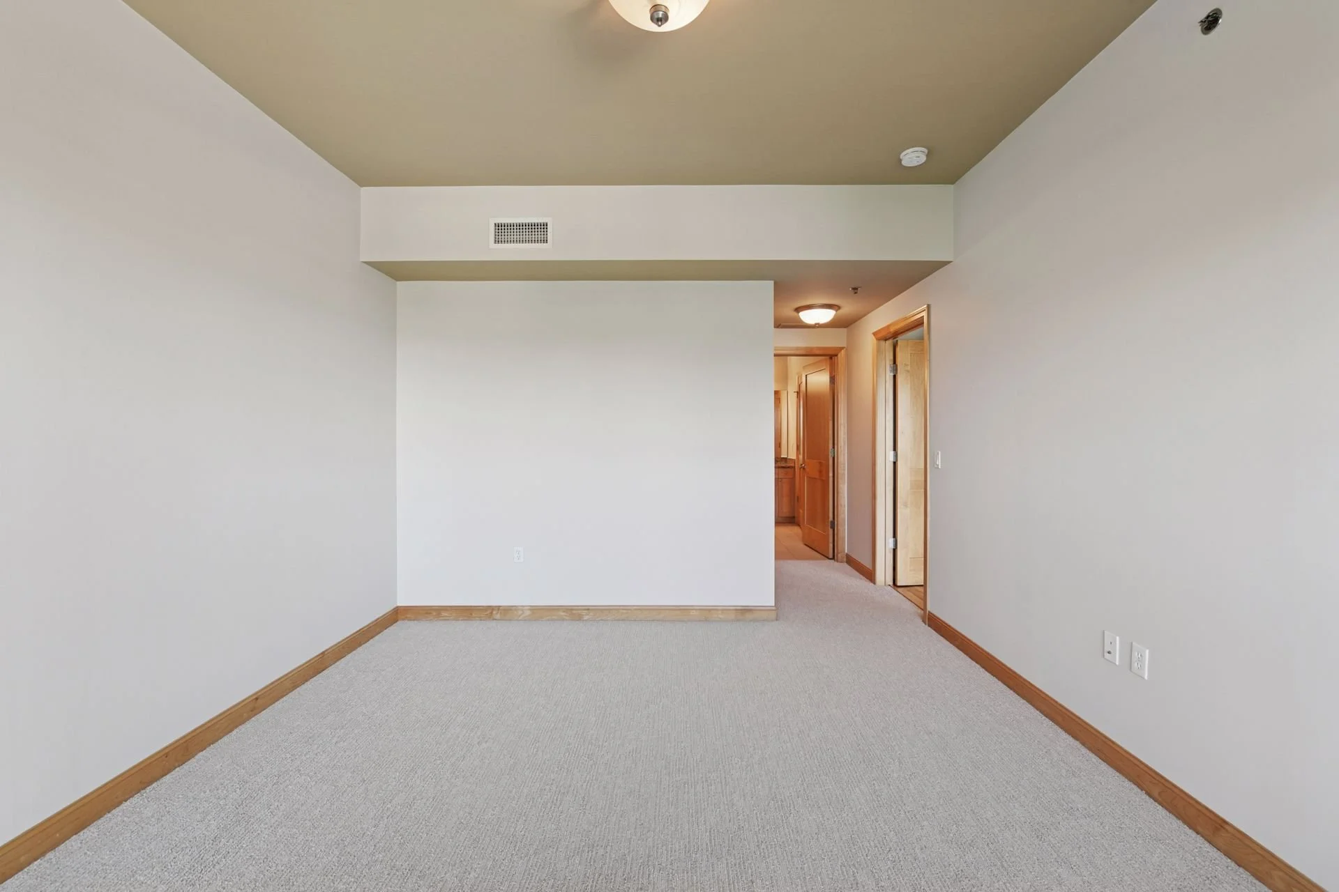 Large bedroom with beige carpet, white walls, wooden trim, and doorways leading to other rooms.