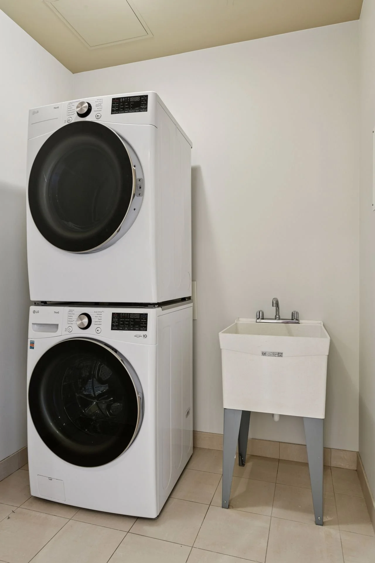 A laundry room with a front-loading washing machine and dryer stacked together, and a utility sink on the right side.