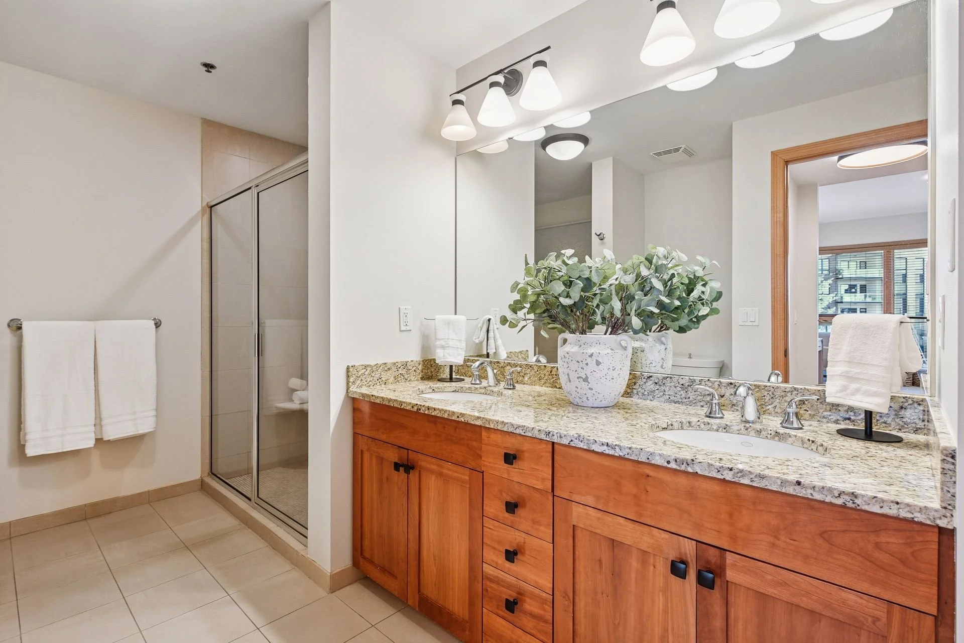 Modern bathroom with granite countertop double sink vanity, large mirror, and glass-enclosed shower.