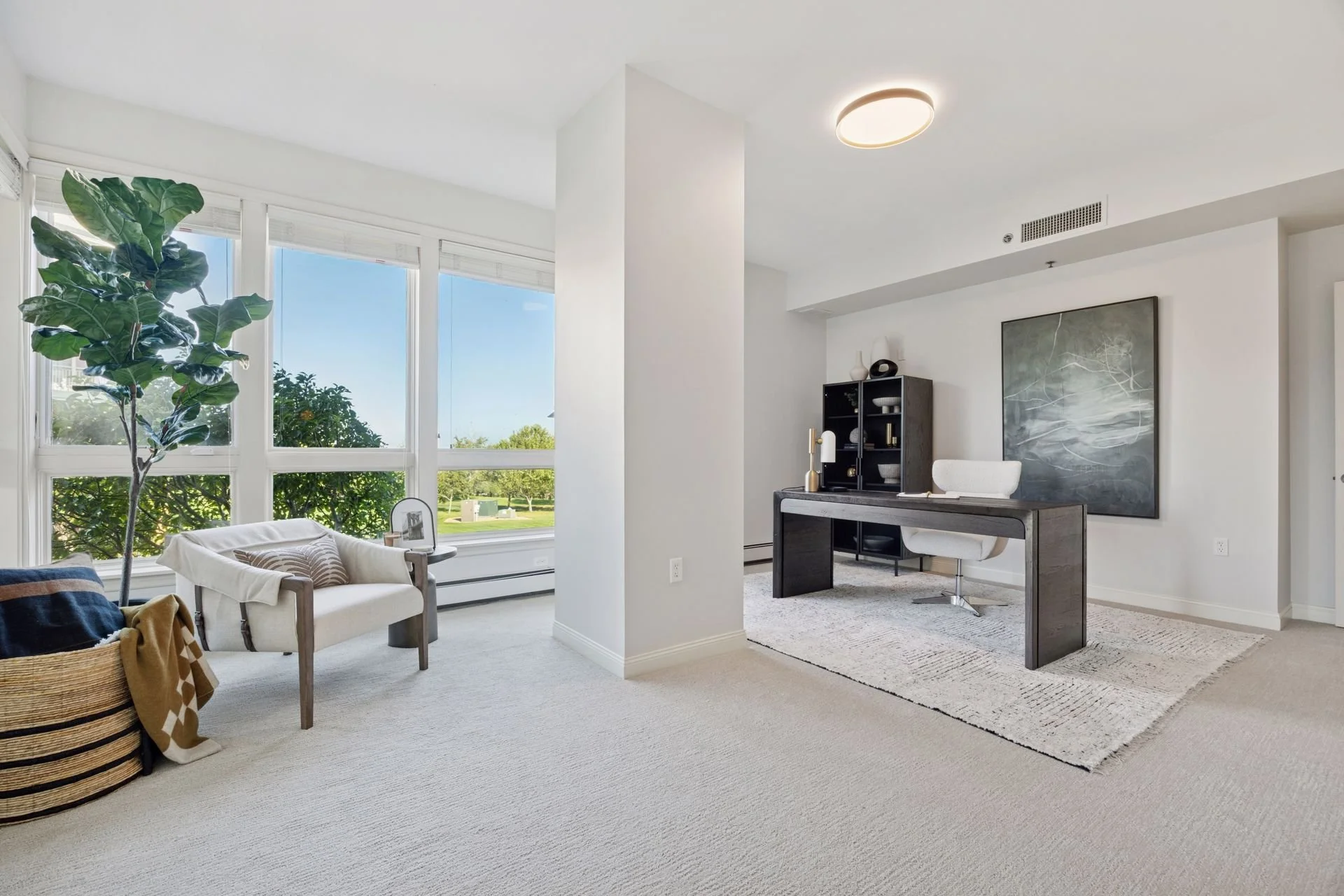 Bright living room with large windows and white walls. The room has a simple, elegant aesthetic with natural light.