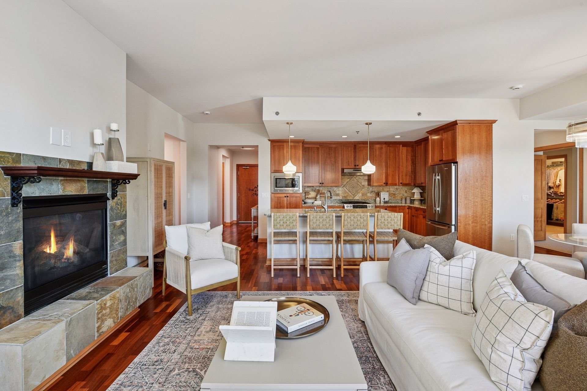 Open living room with fireplace and a view of the kitchen with wooden cabinets, and island.