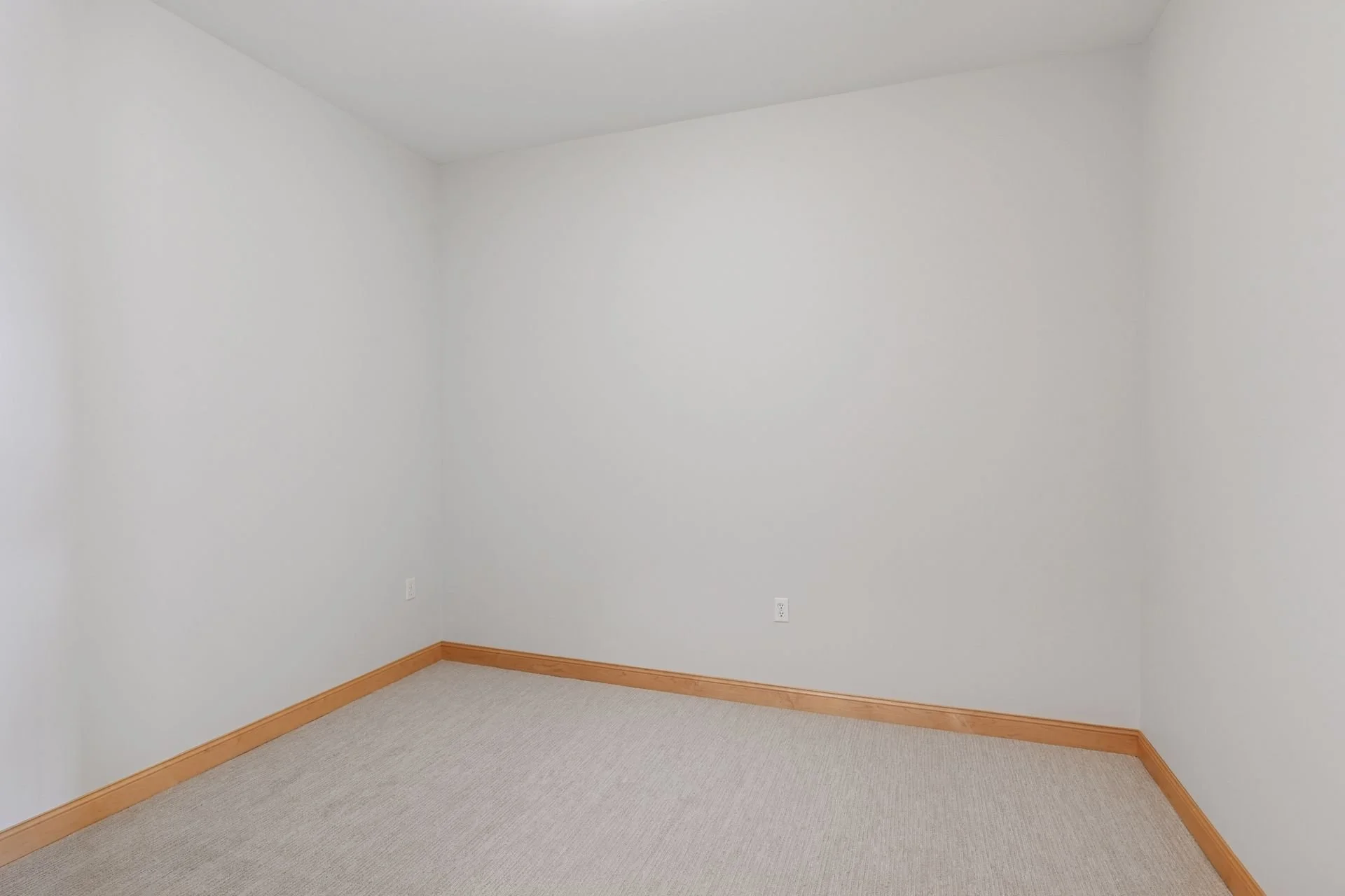 Empty room with white walls, beige carpet, and light wood baseboards.