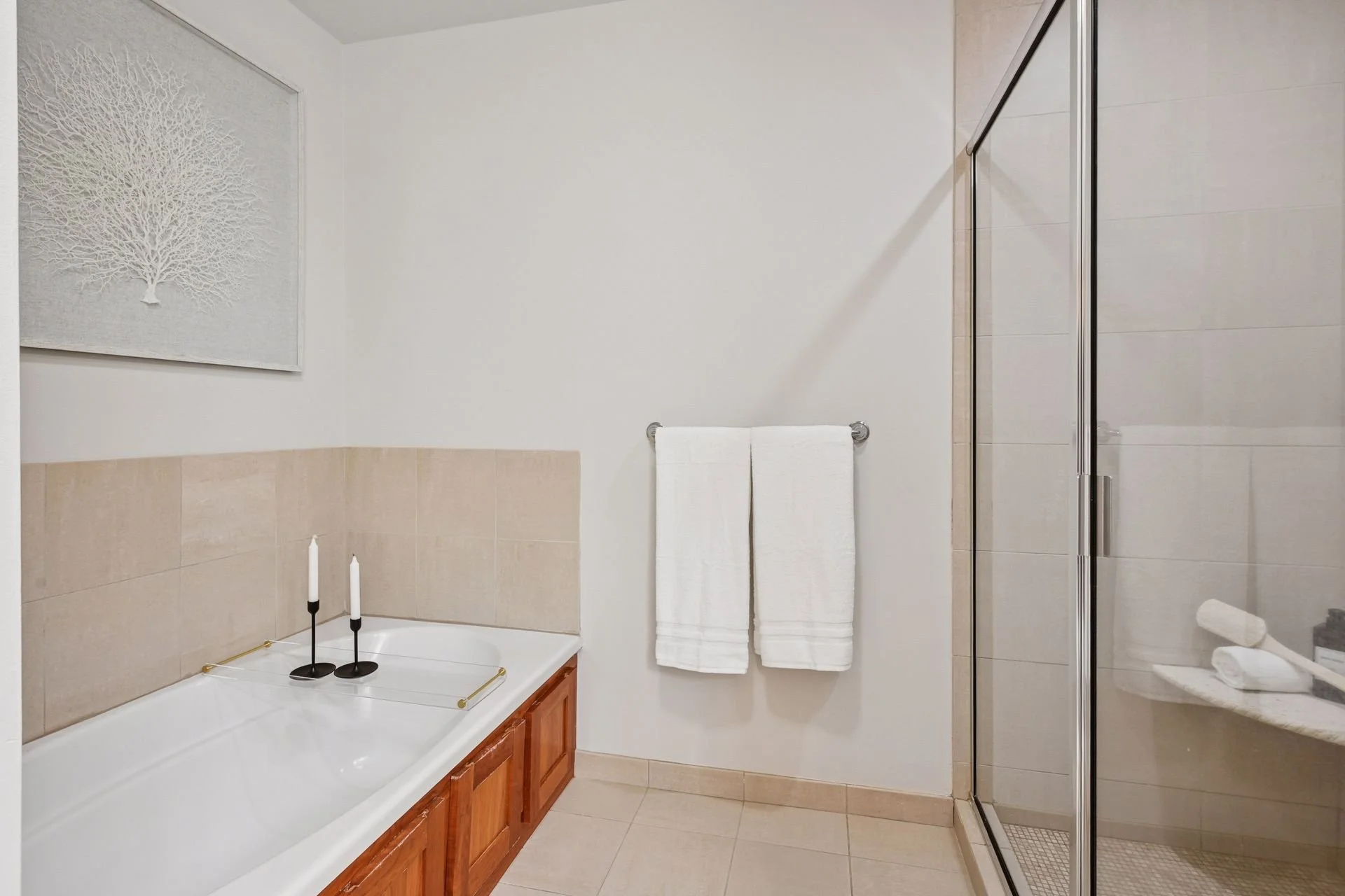 Bathroom with beige tiled floor and walls, white bathtub, a silver towel rack, and an enclosed shower with glass door.